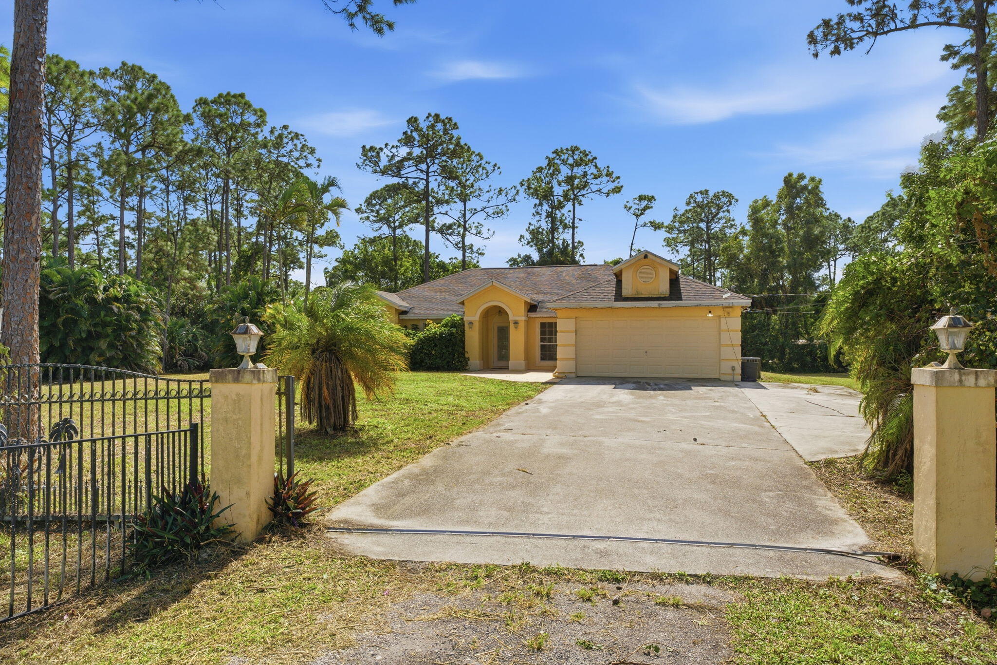 Single-story residence featuring a stucco exterior, concrete driveway, attached garage, arched entryway, and metal perimeter fencing with masonry pillars