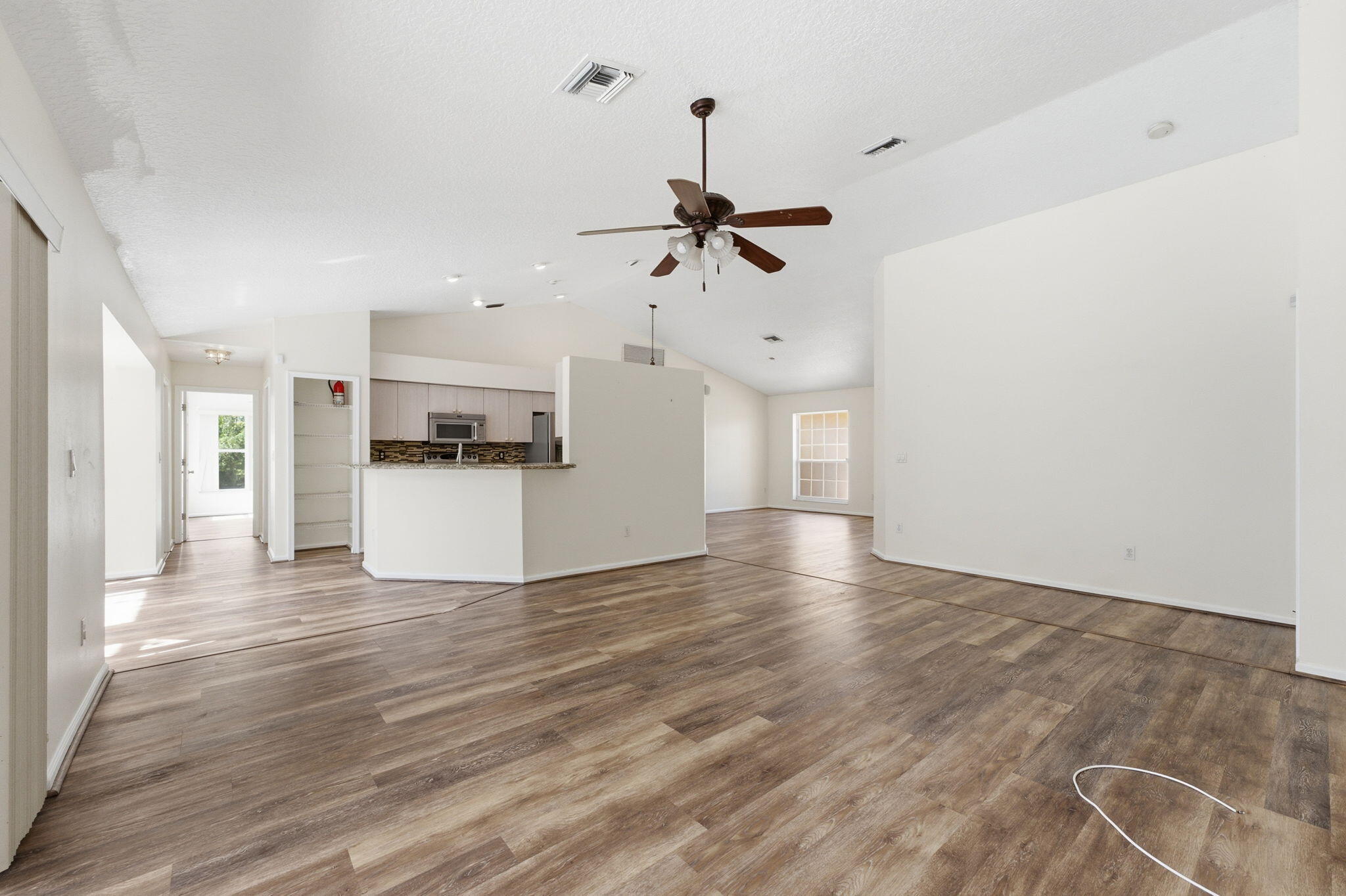 Open-concept floor plan featuring vaulted ceilings, wood-finish flooring, a kitchen breakfast bar, and a ceiling fan with integrated lighting