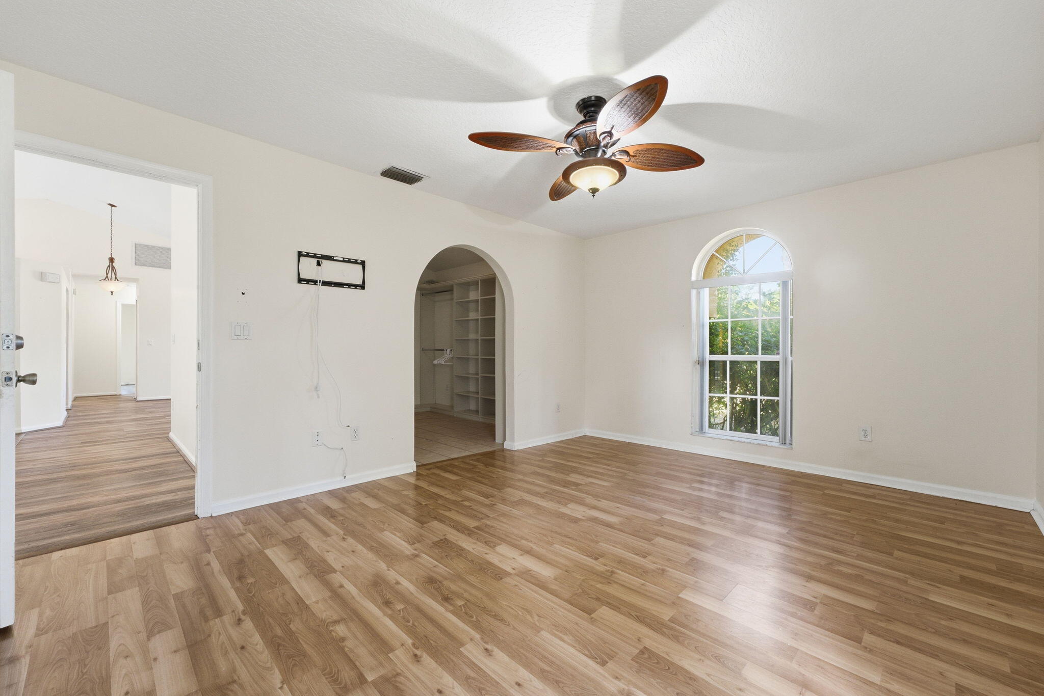 Wood-finish flooring, arched doorway, arched window, and ceiling fan with integrated lighting