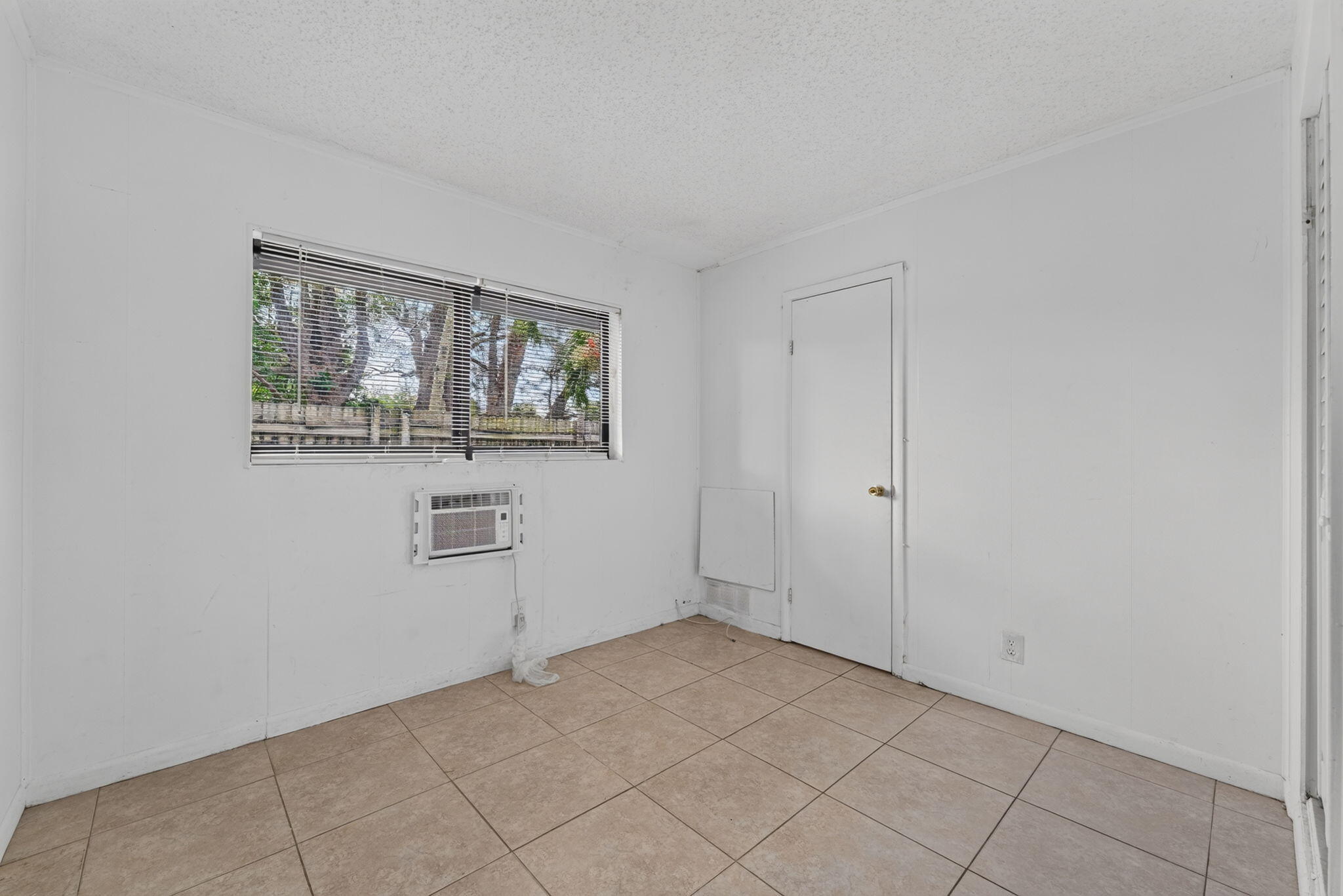 Room featuring neutral tile flooring, horizontal window blinds, and a built-in wall air conditioning unit