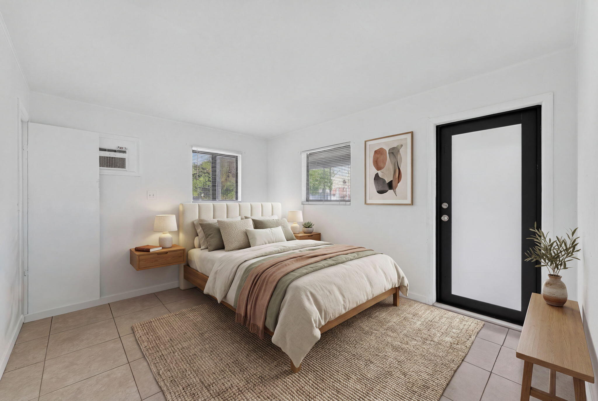 Neutral-toned interior space featuring light-colored tile flooring, multiple windows, and a black-framed exterior door with glass inlay