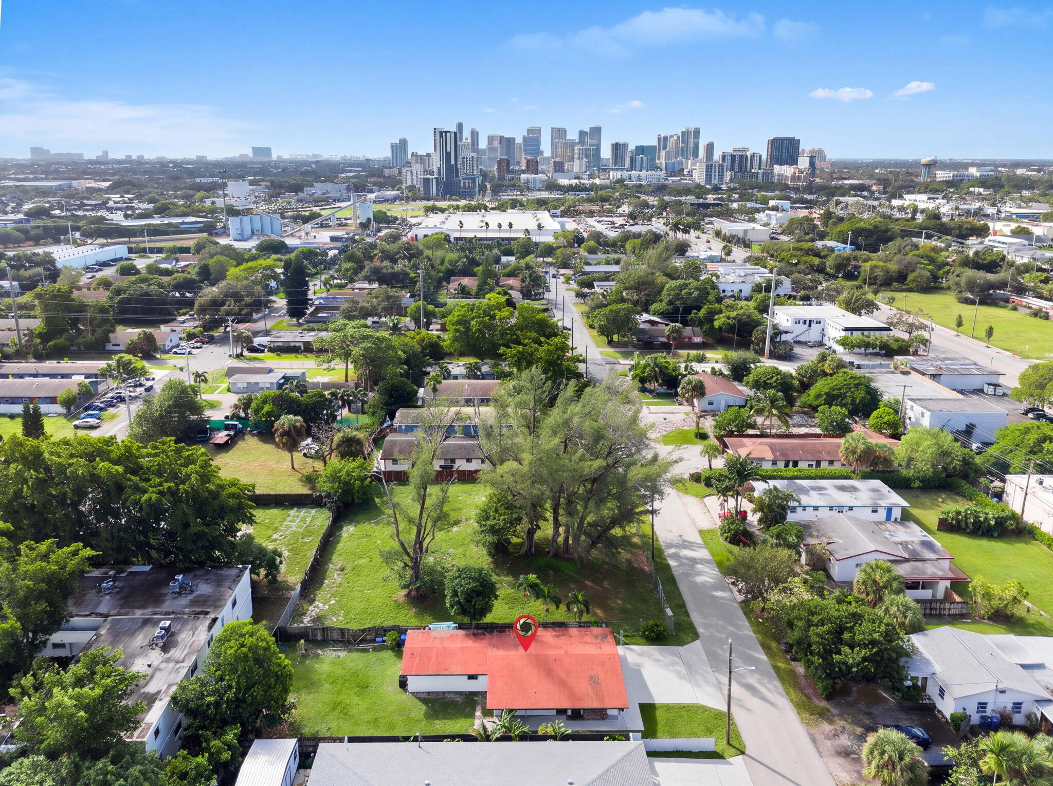 Aerial perspective featuring a red shingle roof, a spacious lot with mature trees, and a metropolitan skyline backdrop