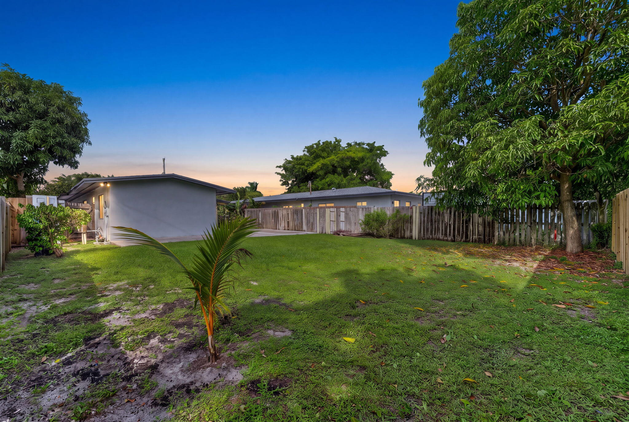 Expansive backyard featuring a level lawn, mature trees, concrete patio space, and wood-style perimeter fencing