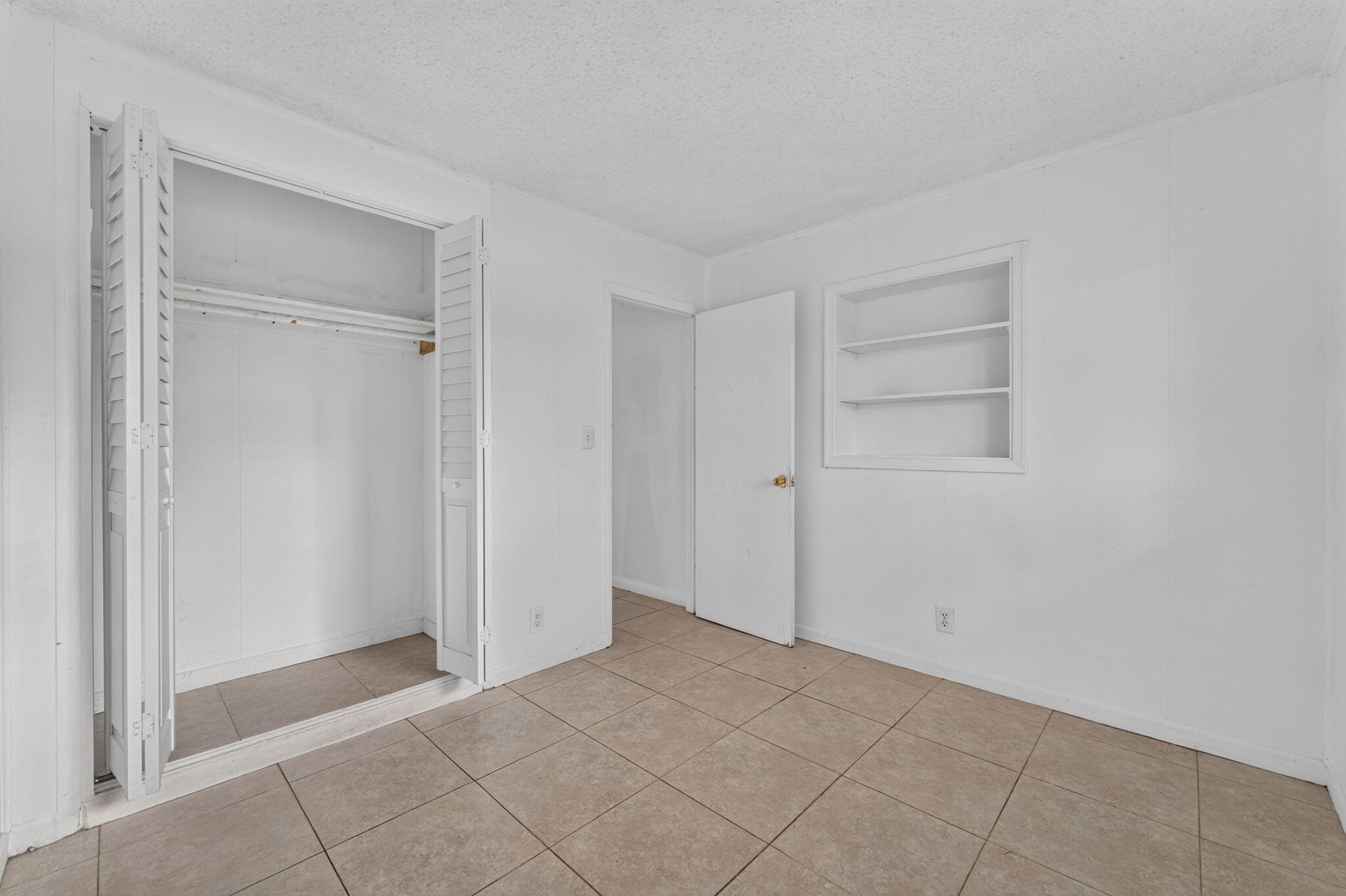 Interior space featuring neutral tile flooring, closet with bi-fold louvered doors, and built-in wall shelving