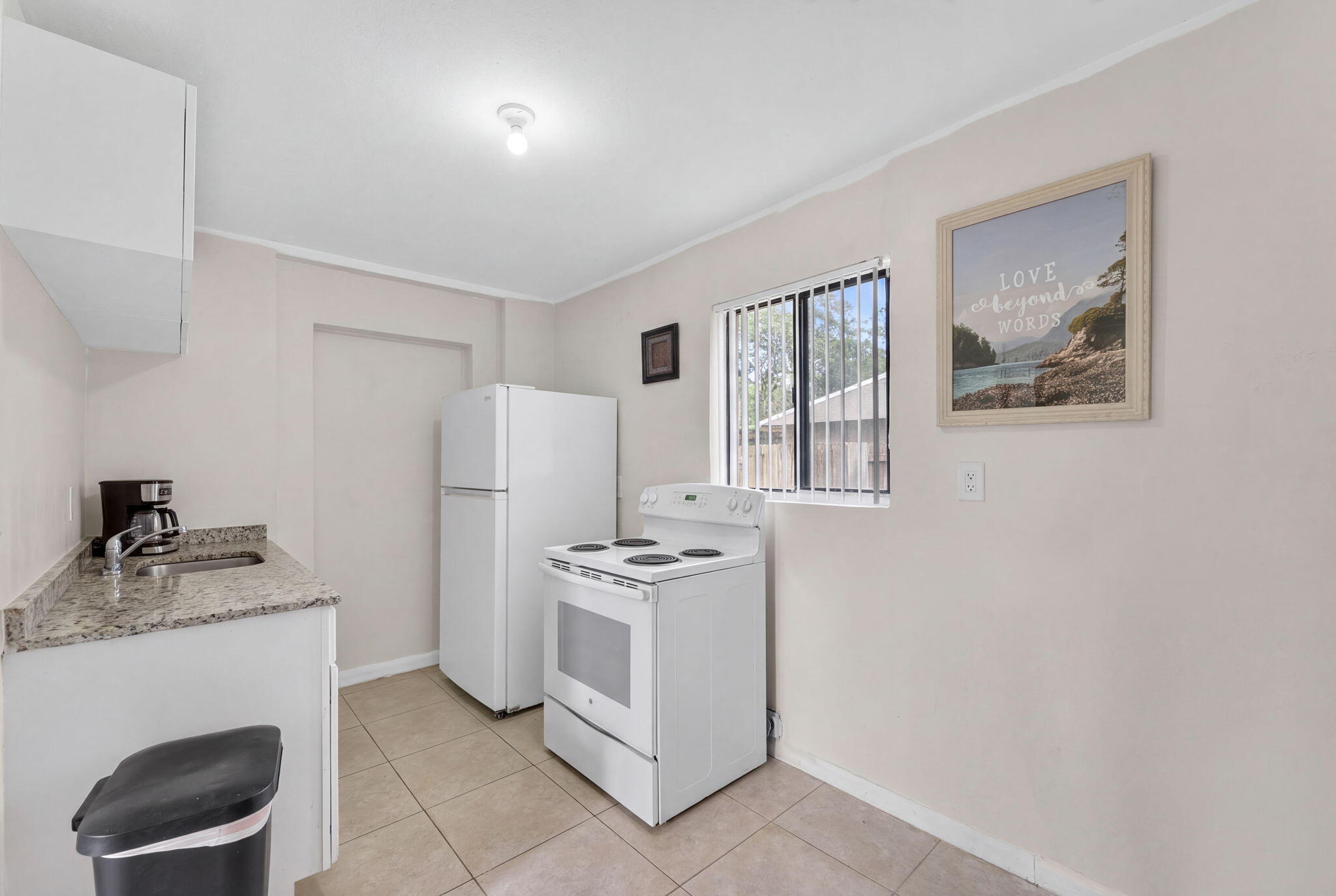 Kitchen featuring stone-finish countertops, tile flooring, white cabinetry, and a window with horizontal blinds
