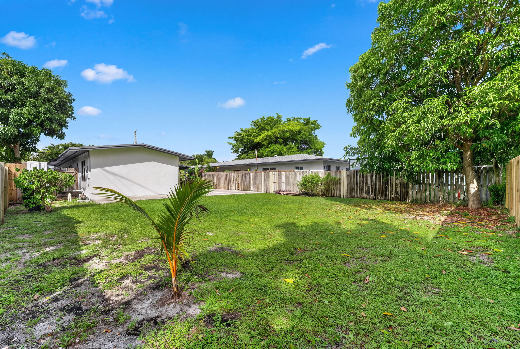Expansive backyard featuring a sprawling lawn, mature trees, concrete patio, and a perimeter wood privacy fence