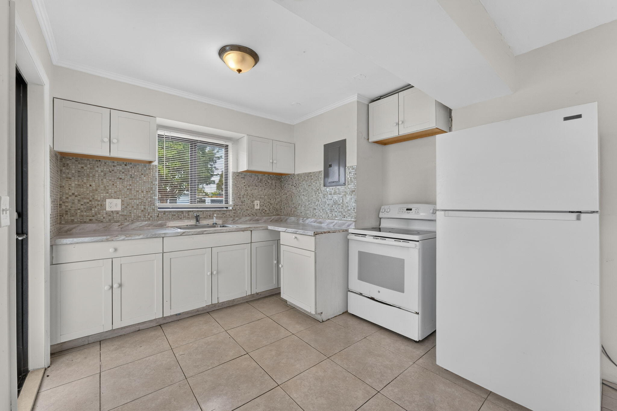 Kitchen featuring white cabinetry, stone-texture backsplash, neutral-toned tile flooring, and white appliance suite