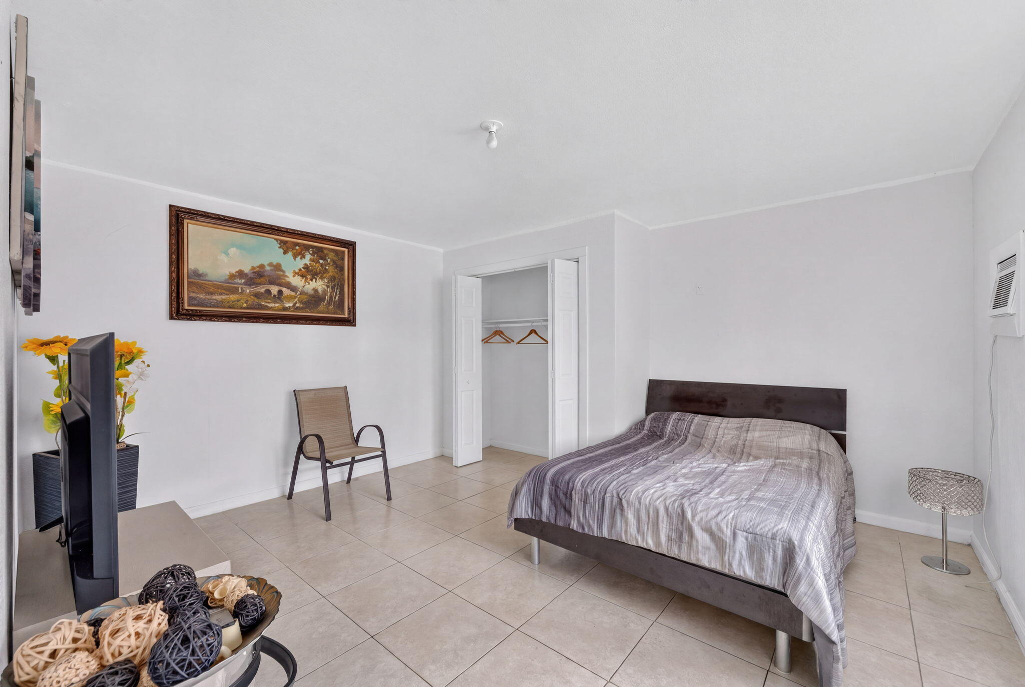 Room with neutral walls, large-format tile flooring, and a built-in closet with folding doors
