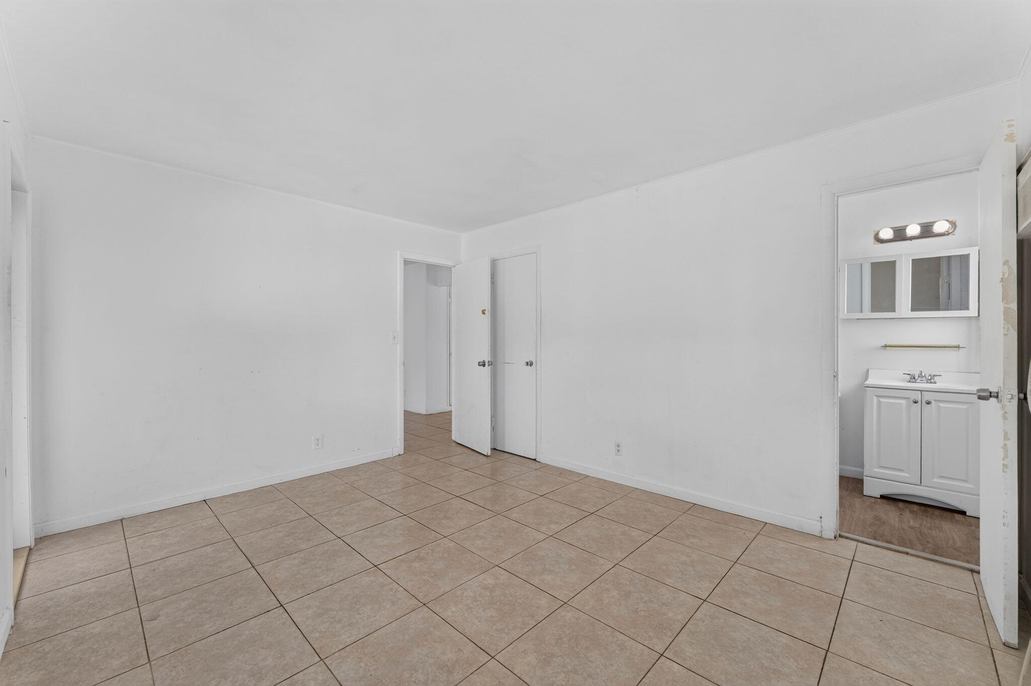 Neutral-toned tile flooring throughout with a dual-door closet and access to a bathroom featuring a white vanity cabinet and a wall-mounted mirrored medicine cabinet