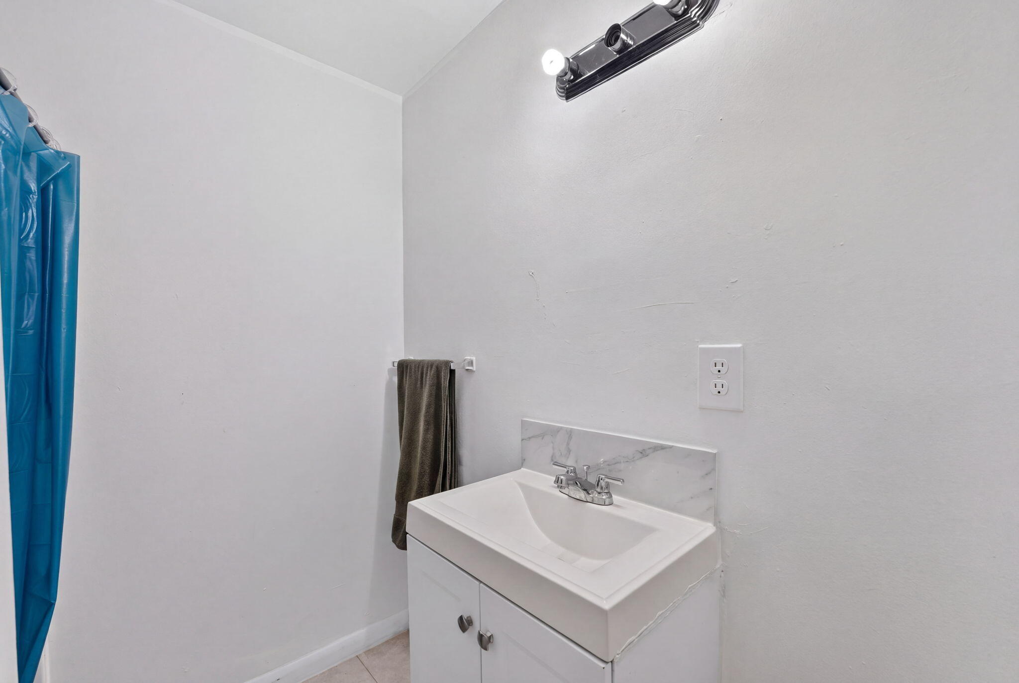 Bathroom vanity featuring a white cabinet, integrated sink, stone-finish backsplash, and a multi-bulb wall-mounted light fixture