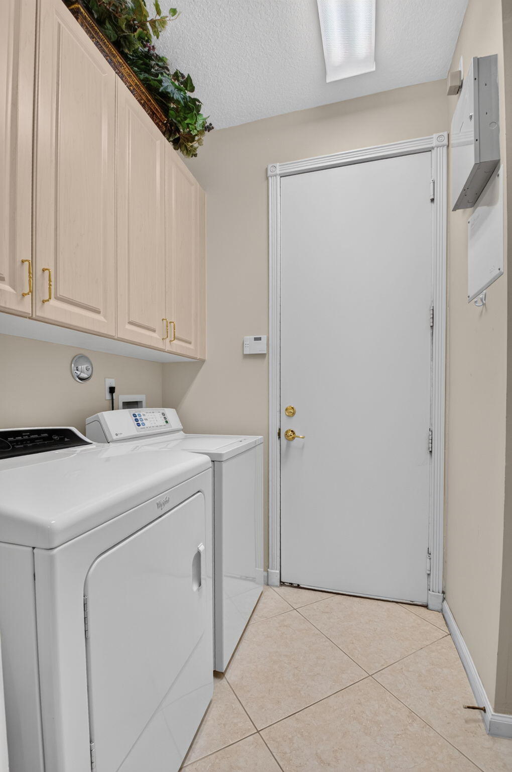Laundry area featuring light-toned cabinetry with brass-finish hardware, tile flooring, and a solid-panel door