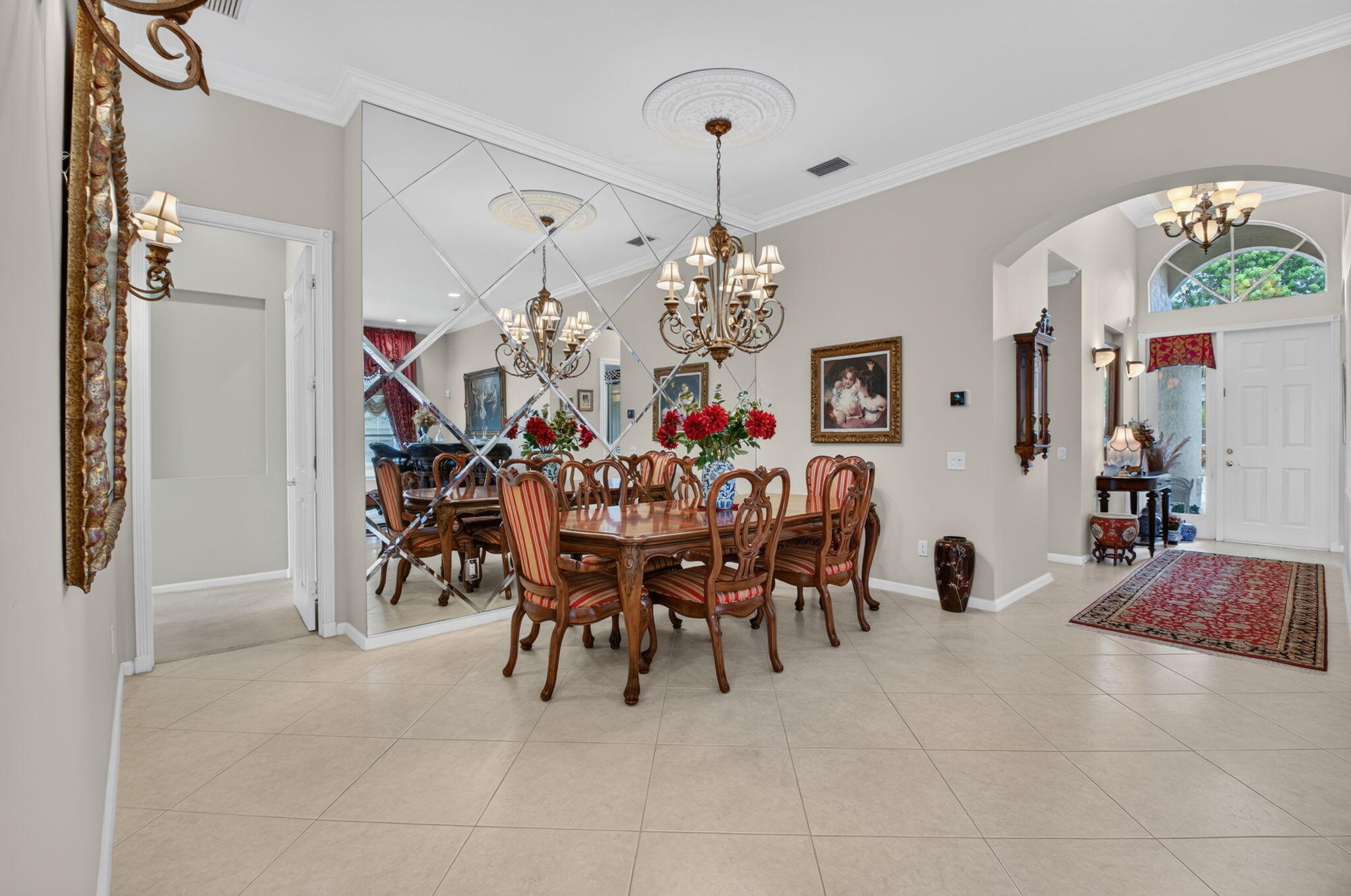 Formal dining area featuring diamond-patterned wall mirrors, crown molding, arched entryways, tile flooring, and a decorative ceiling medallion with a multi-light chandelier