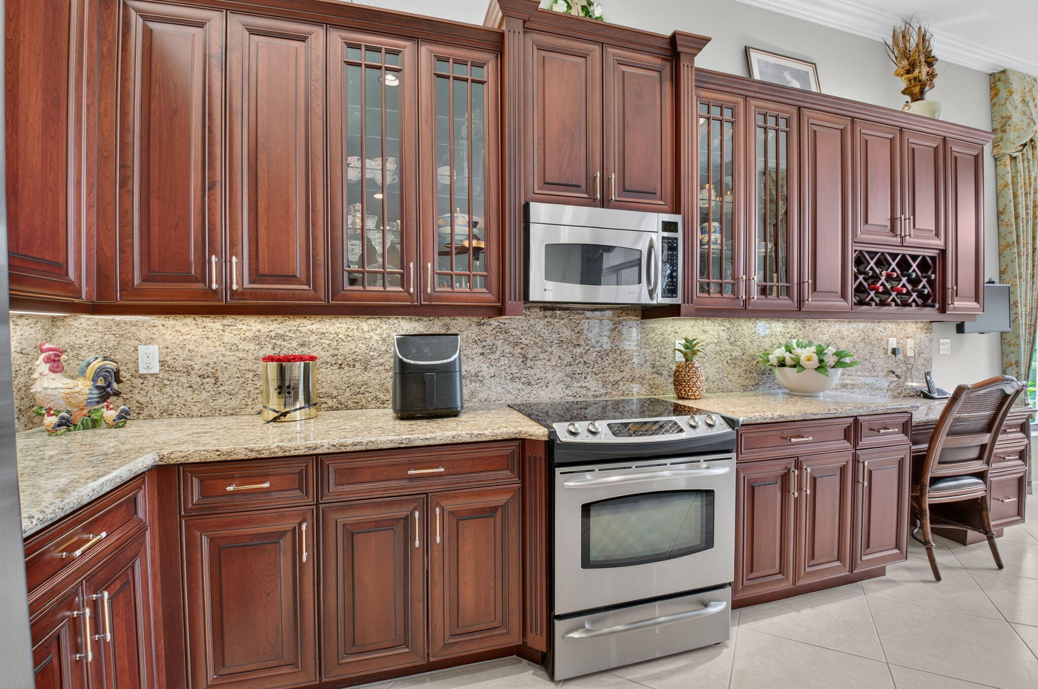 Kitchen featuring rich-toned cabinetry with glass-paneled accents, stone countertops, stone tile backsplash, integrated wine storage, and stainless steel appliances