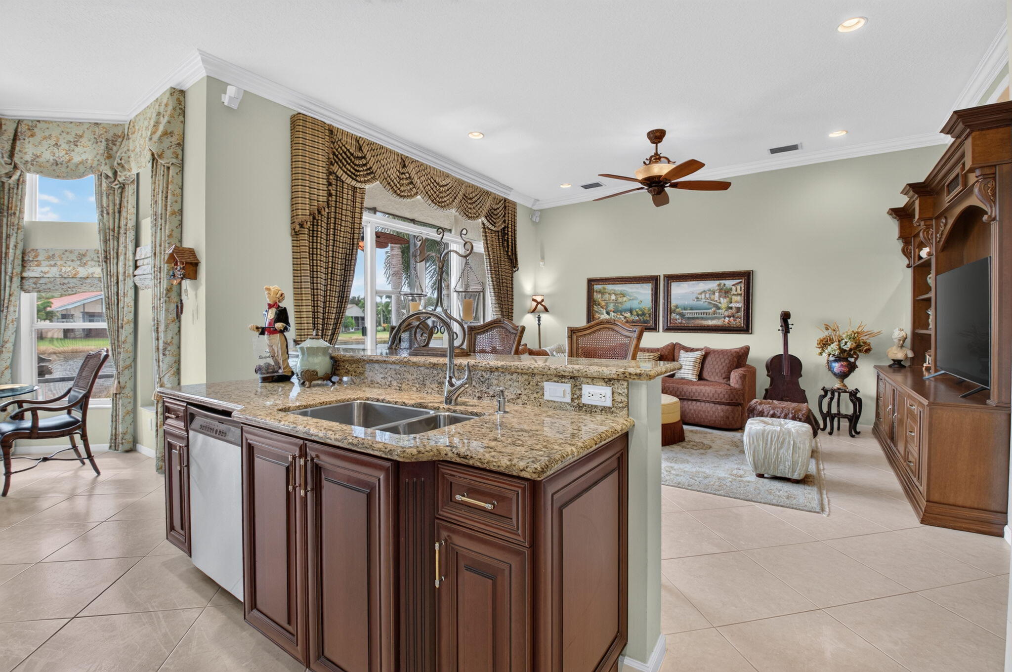 Kitchen featuring dark wood cabinetry, stone-surface countertops, a dual-basin stainless steel sink, large-format tile flooring, and a built-in wood entertainment console