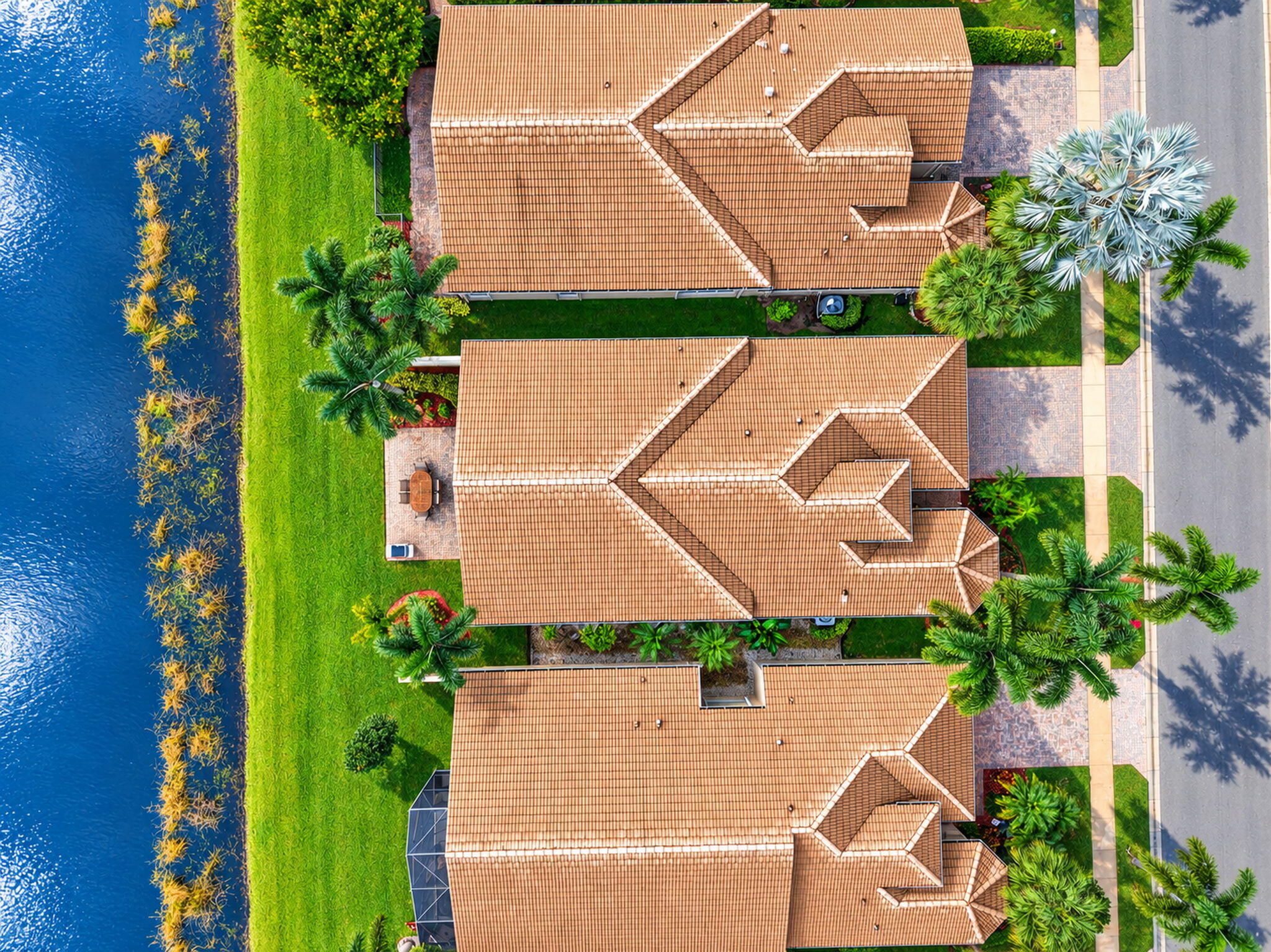 Waterfront property featuring tile roofing, brick-paved driveways, and mature landscaping