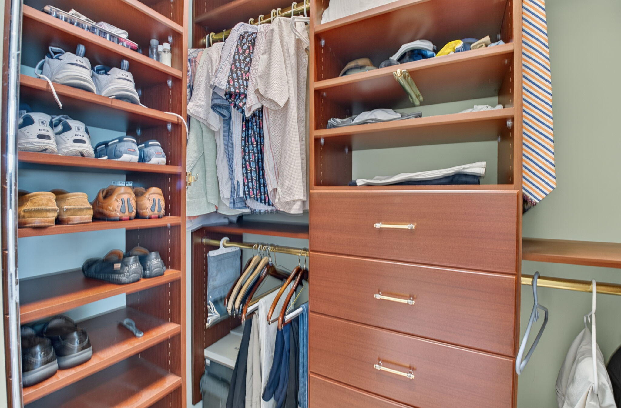 Built-in wooden closet system featuring multiple open shelving units, integrated hanging rods, and a four-drawer dresser with metallic pulls