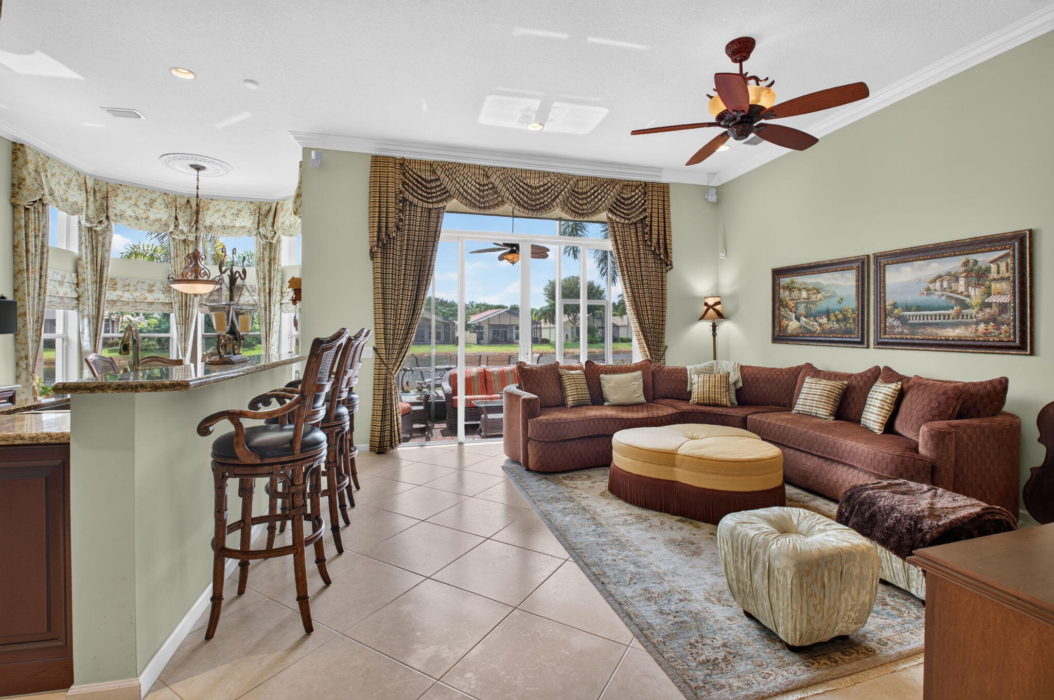 Open-concept area featuring stone-surfaced breakfast bar, large-format tile flooring, crown molding, ceiling fan with integrated lighting, and expansive glass sliding doors