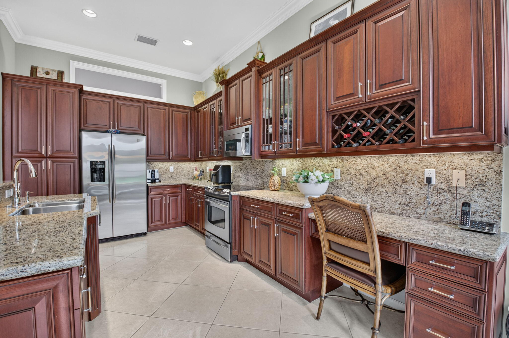 Kitchen featuring cherry-tone cabinetry, stone countertops, stainless steel appliances, a built-in wine rack, and a dedicated desk workspace