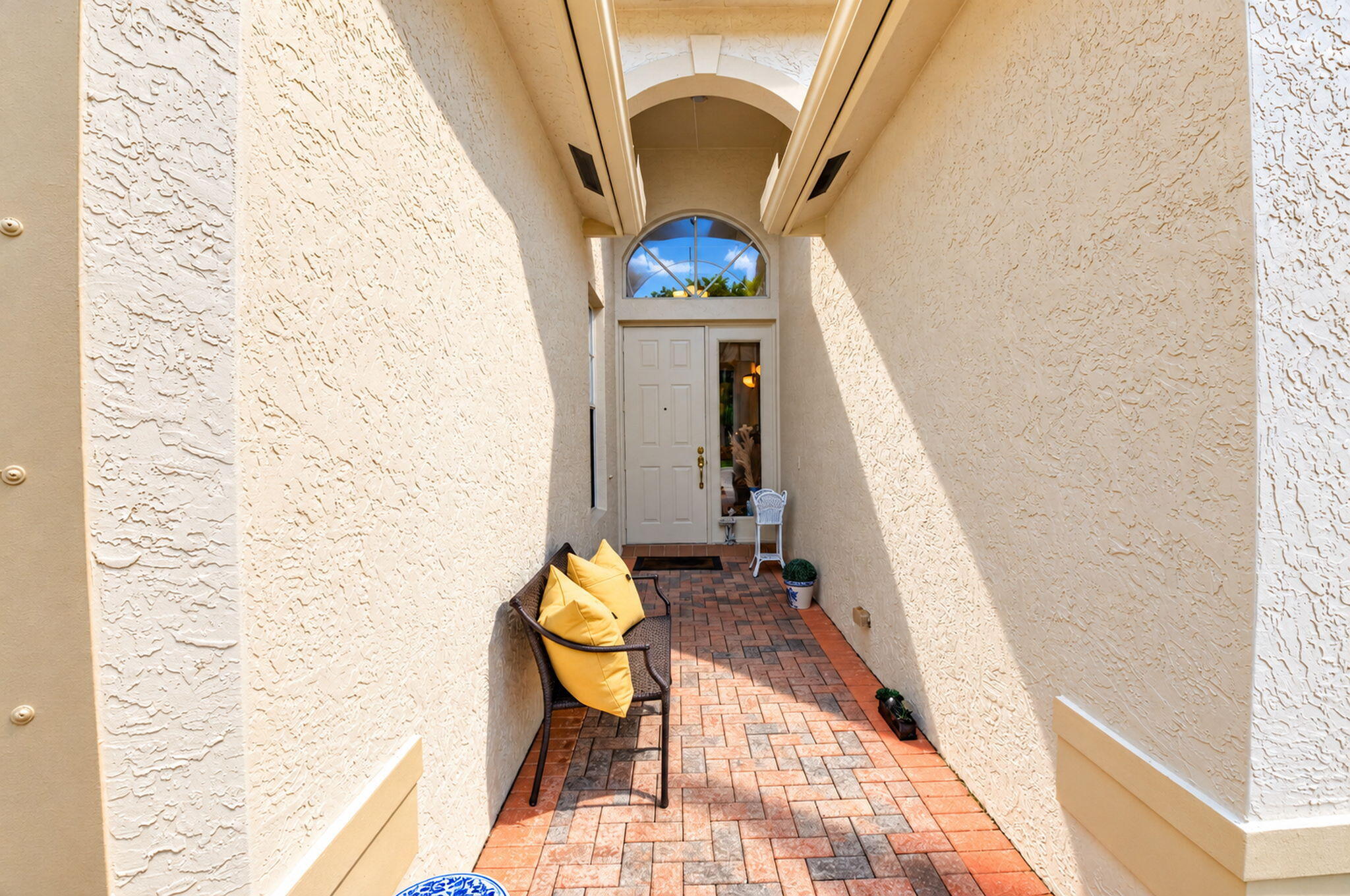 Covered entryway featuring textured stucco exterior walls, brick-paver flooring, an arched entry detail, and a multi-pane door with an arched transom window