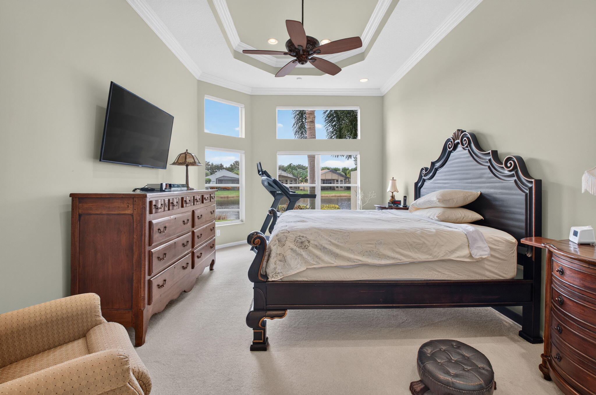 Tray ceiling with crown molding, ceiling fan, carpeted flooring, and a bay window featuring multi-pane glass