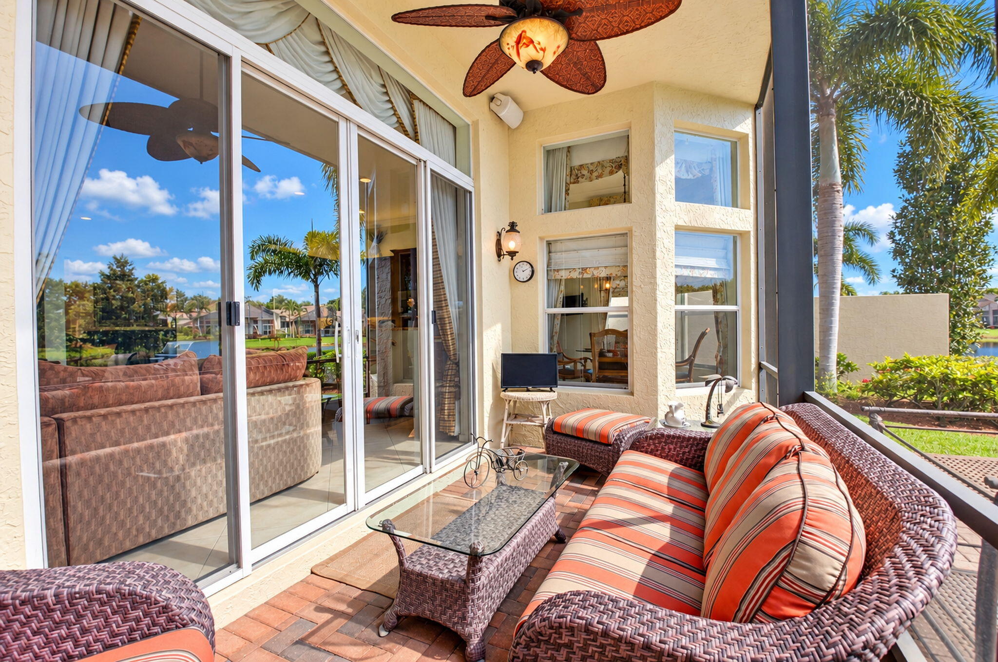 Screened-in lanai featuring paver flooring, a ceiling fan with leaf-shaped blades, and expansive sliding glass doors