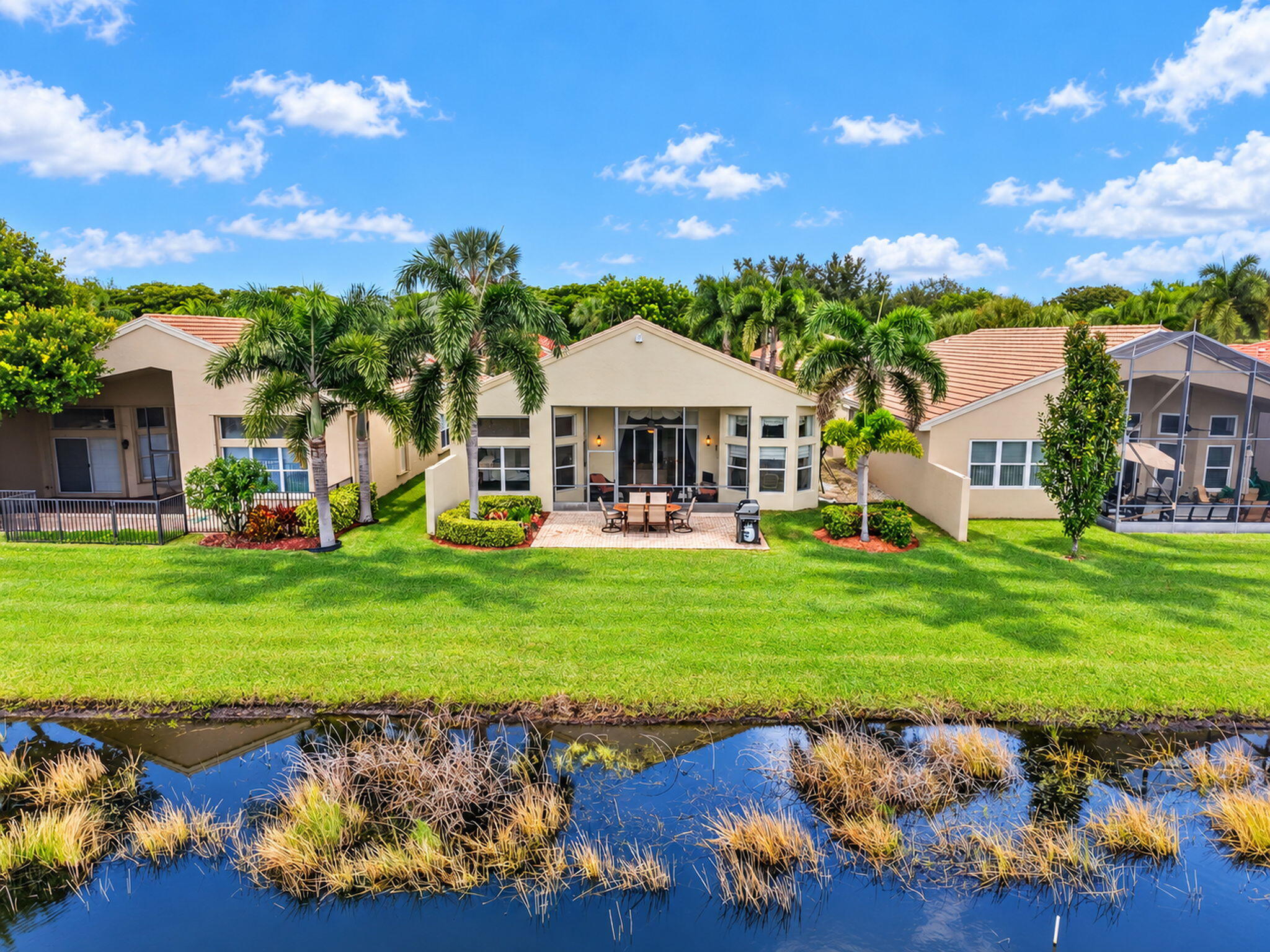 Waterfront property featuring a concrete paver patio, stucco exterior, tile roofing, and mature palm trees