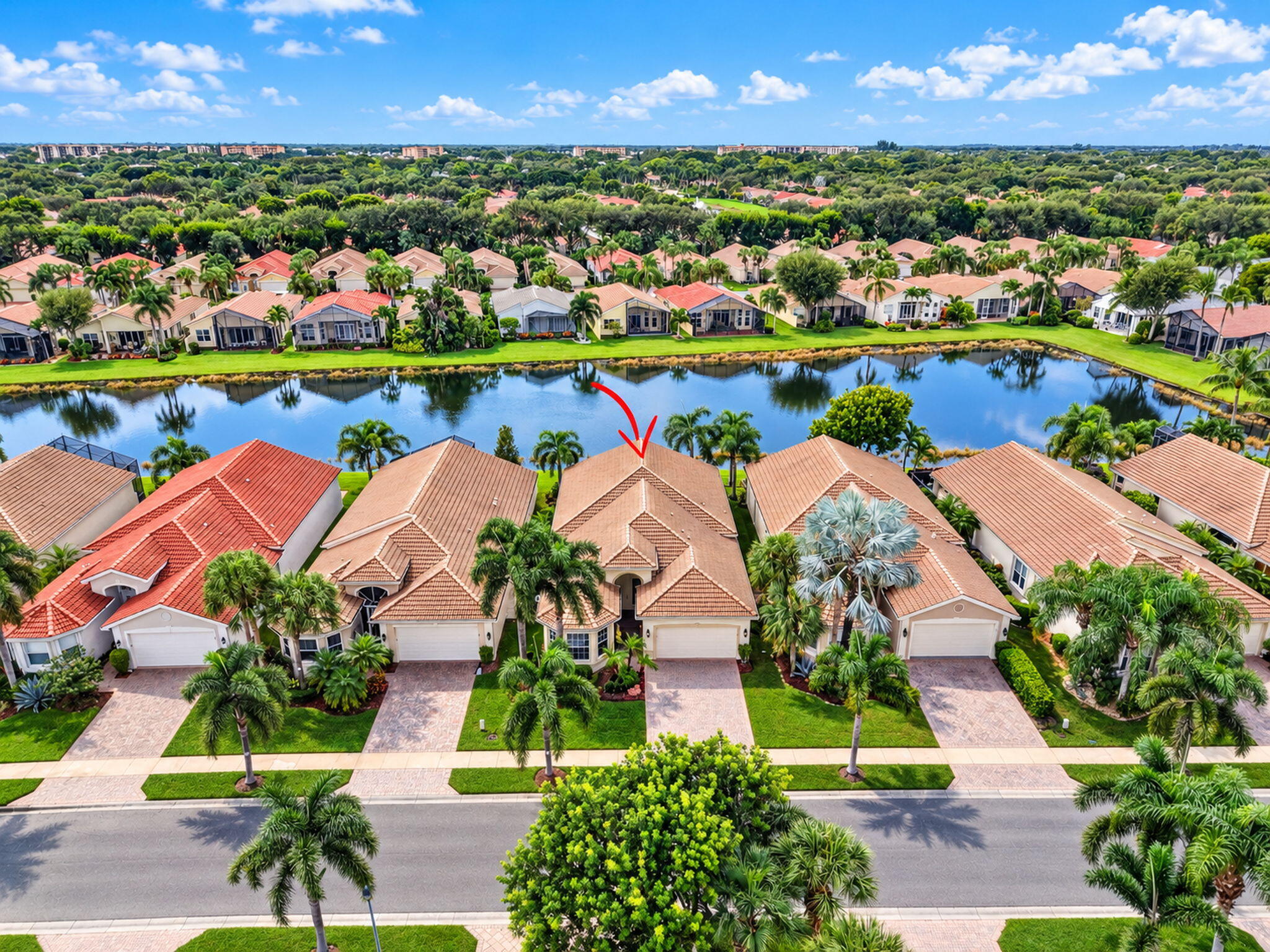 Single-story residence featuring a tile roof, paved driveway, mature palm landscaping, and water frontage