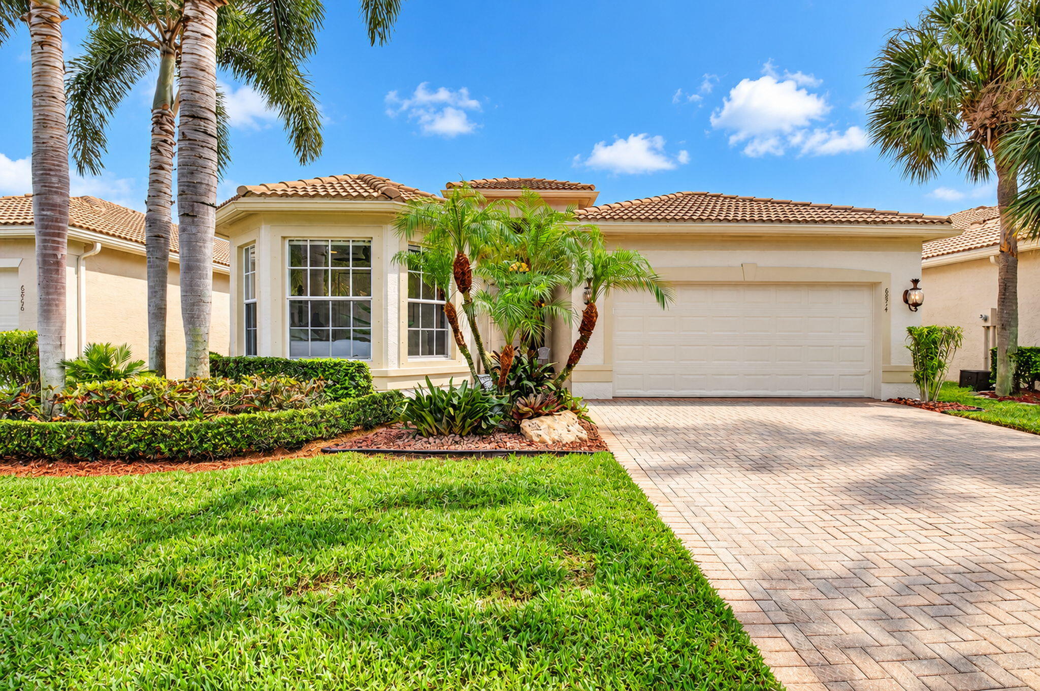 Stucco exterior featuring a tile roof, bay window, paved driveway, and curated tropical landscaping Stucco exterior featuring a tile roof, bay window, paved driveway, and curated tropical landscaping