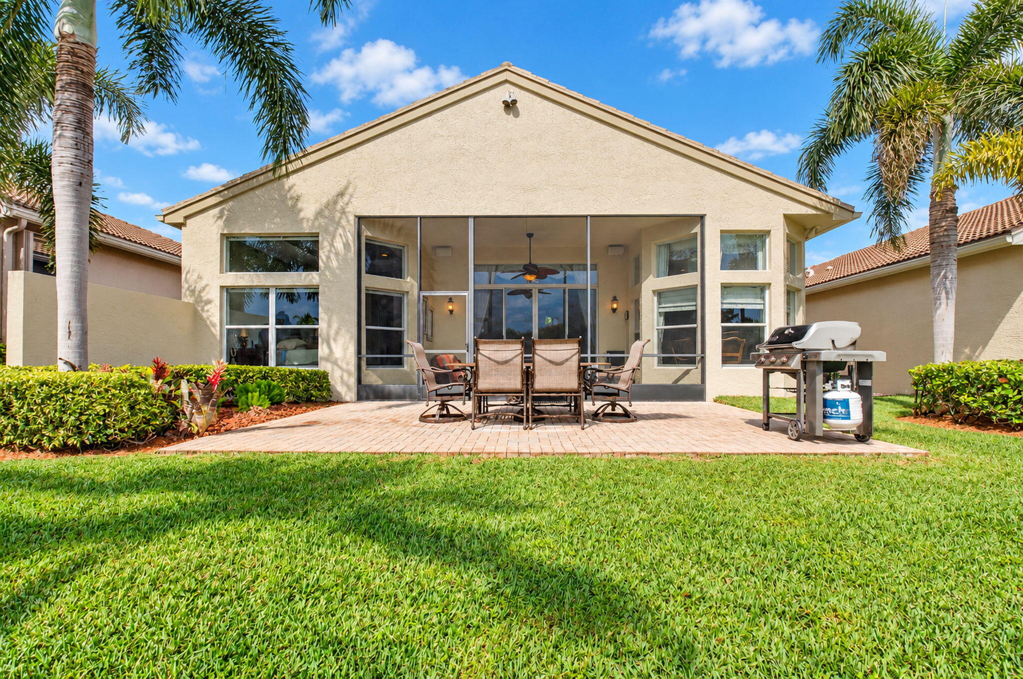 Stucco exterior featuring a screened-in lanai, paver patio, and manicured lawn with room for a pool