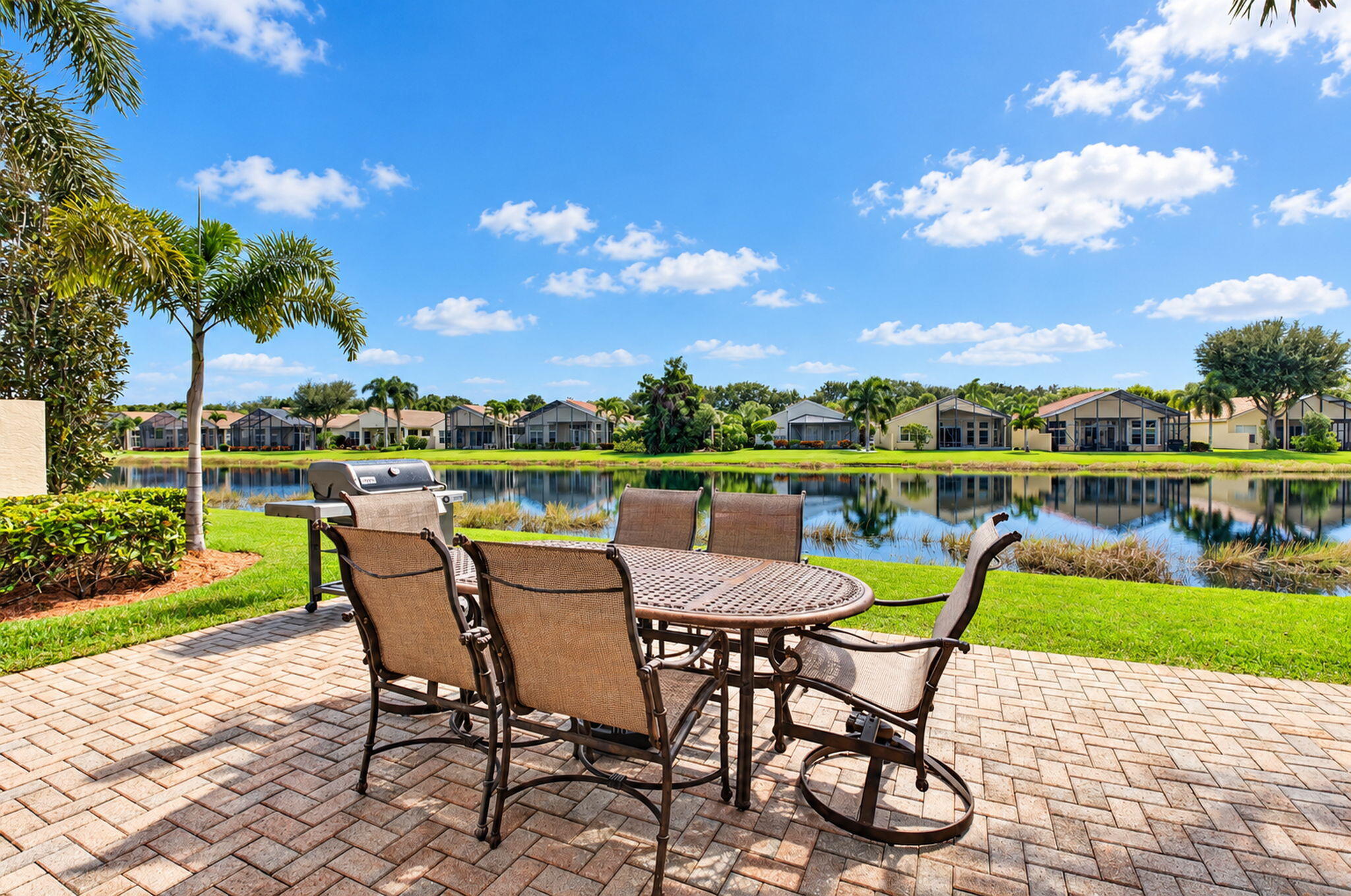 Paver patio featuring a manicured lawn, lake frontage, and mature palm trees