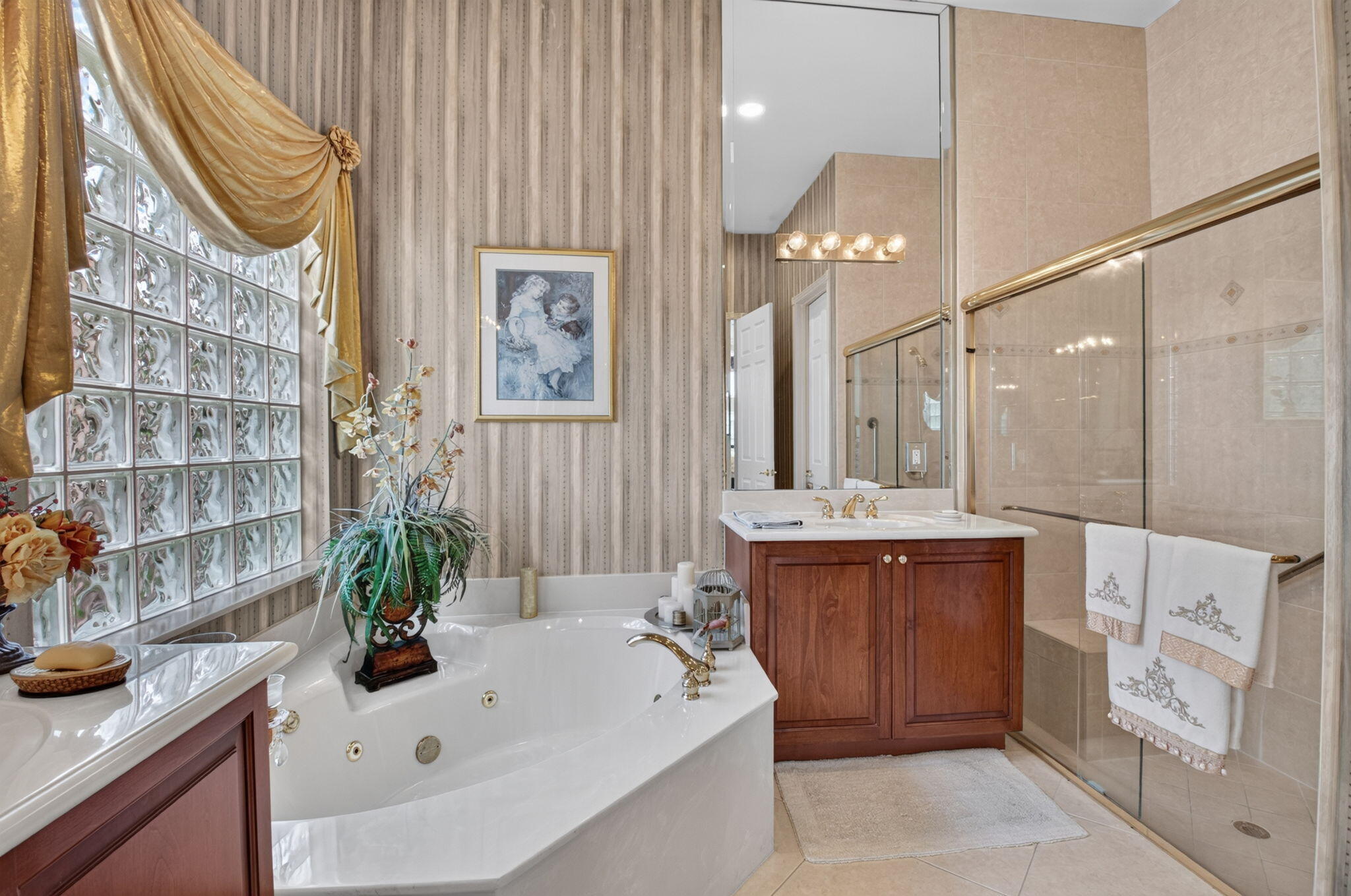 Bathroom featuring a jetted corner soaking tub, glass block window, wood vanity with a stone countertop, and a walk-in shower with a glass enclosure