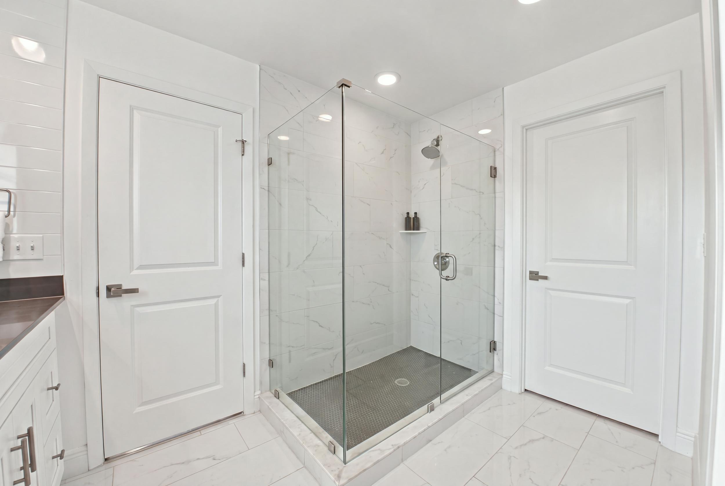 Glass-enclosed shower with stone-finish surround, recessed lighting, and built-in closet system featuring dark cabinetry with integrated shelving and drawers