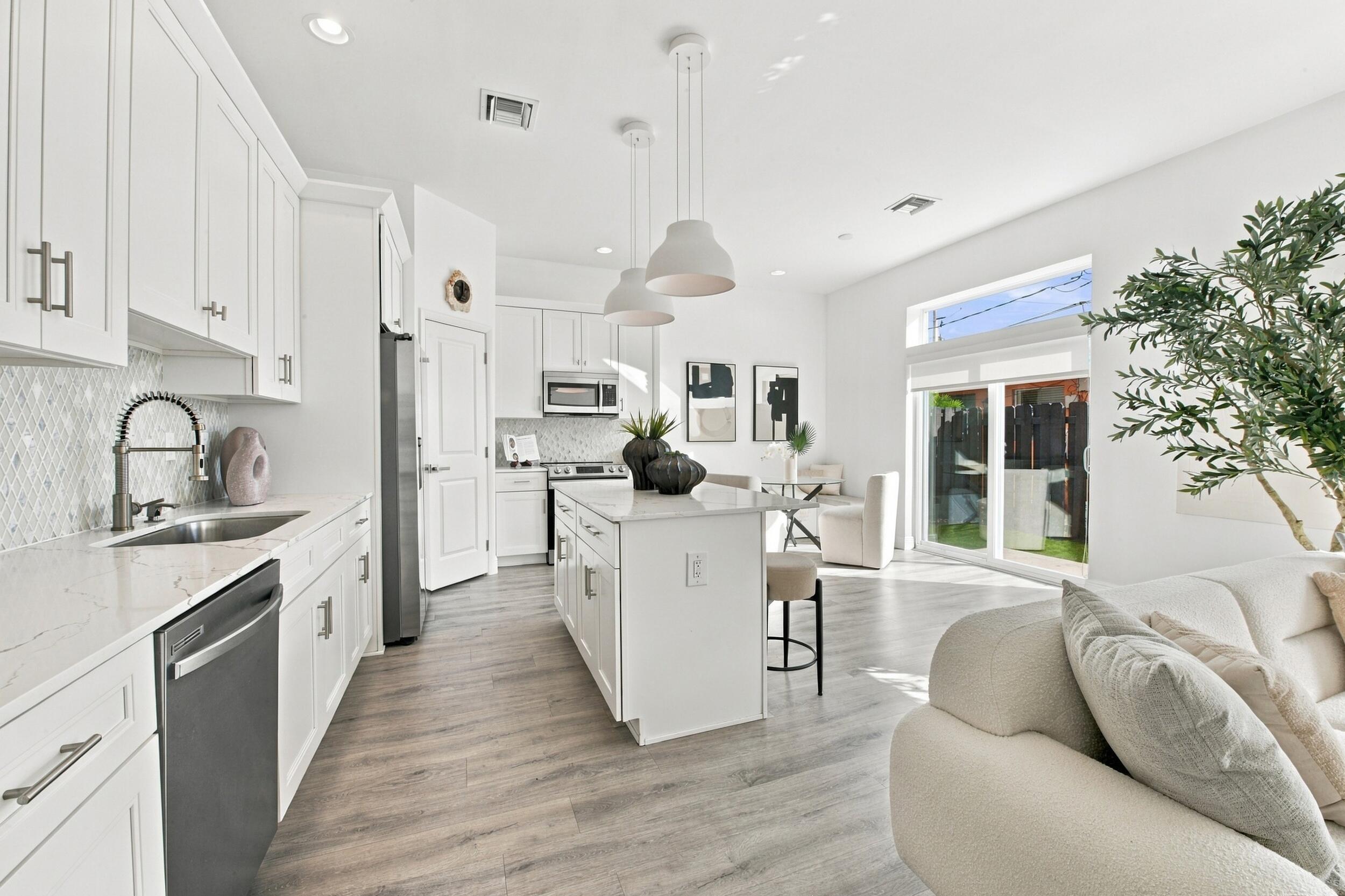 Kitchen featuring white cabinetry, quartz countertops, a central island with pendant lighting, stainless steel appliances, and wood-finish flooring Kitchen featuring white cabinetry, quartz countertops, a central island with pendant lighting, stainless steel appliances, and wood-finish flooring