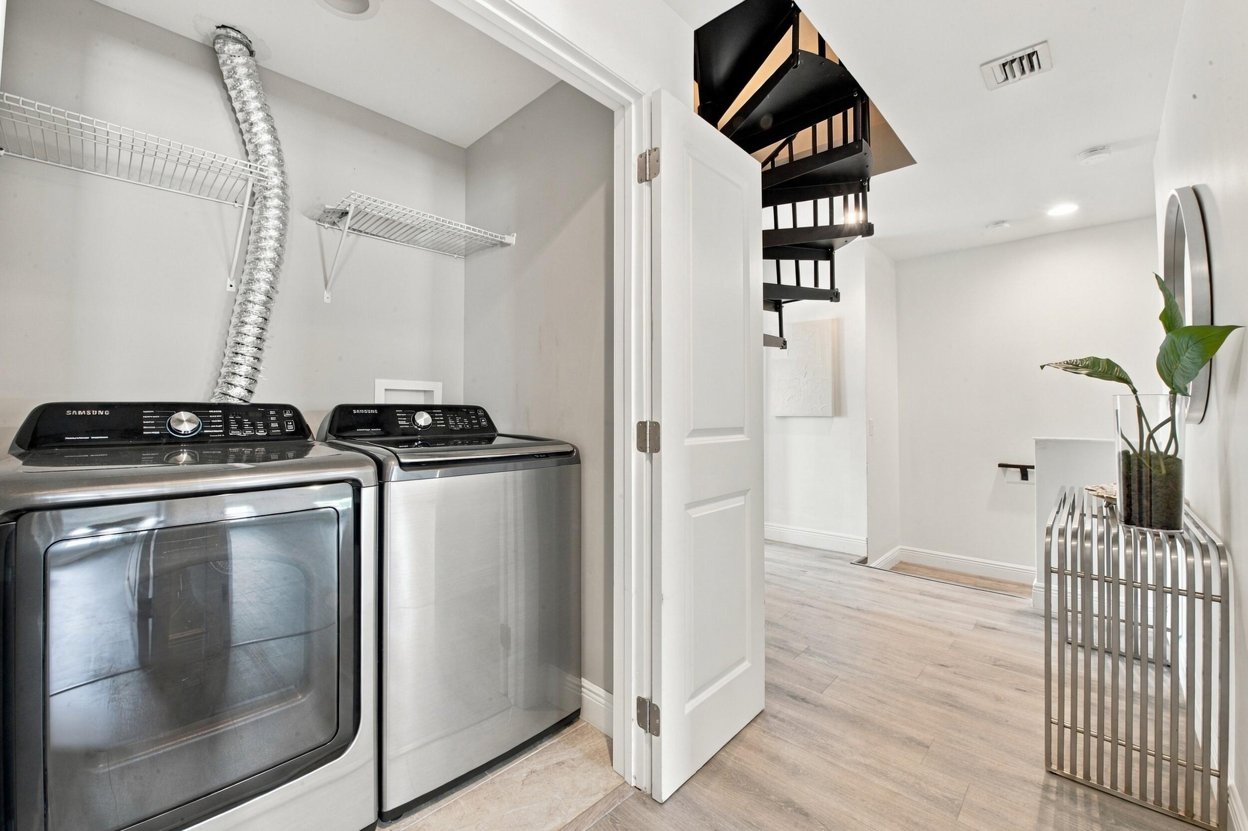 Laundry area featuring stainless steel appliances and wire shelving, wood-finish flooring, and a spiral staircase with metal railings