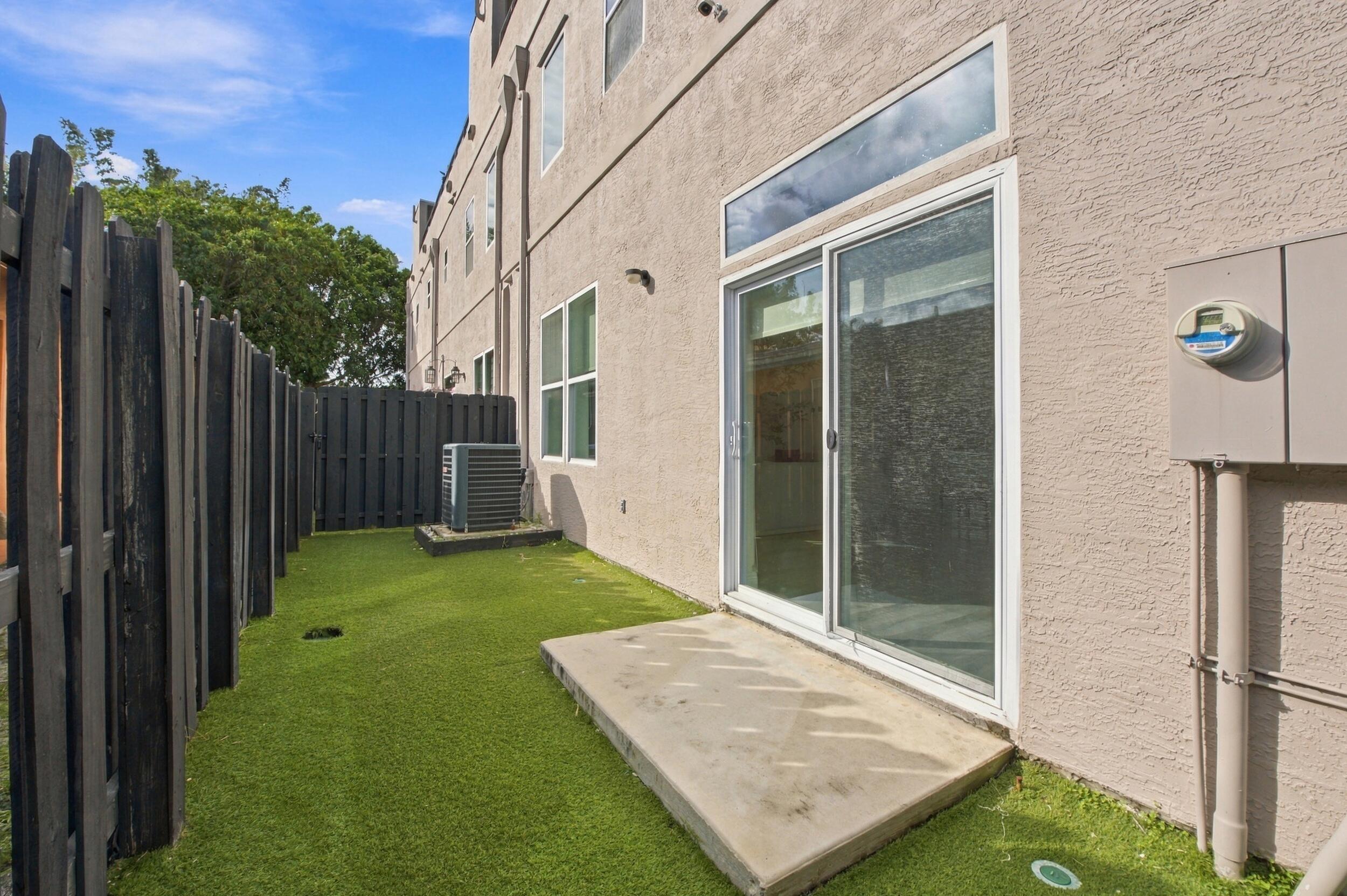 Private rear courtyard featuring a concrete patio, synthetic turf lawn, and dark-finished vertical privacy fencing