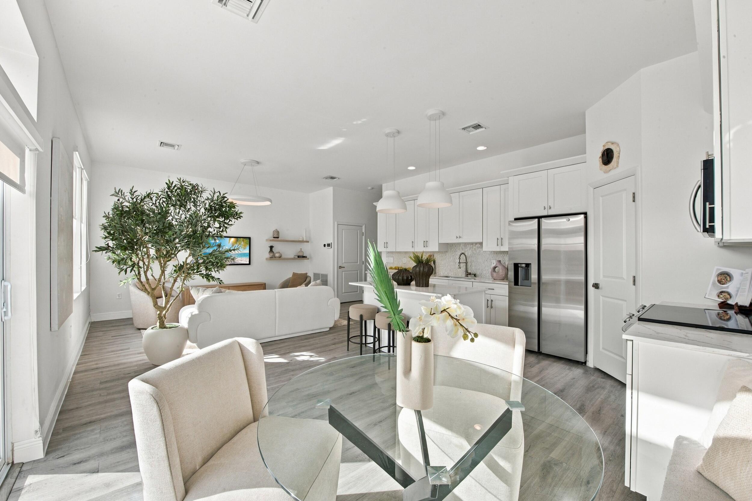 Open-concept kitchen featuring white shaker-style cabinetry, quartz countertops, a waterfall-edge center island, stainless steel appliances, and wood-finish flooring