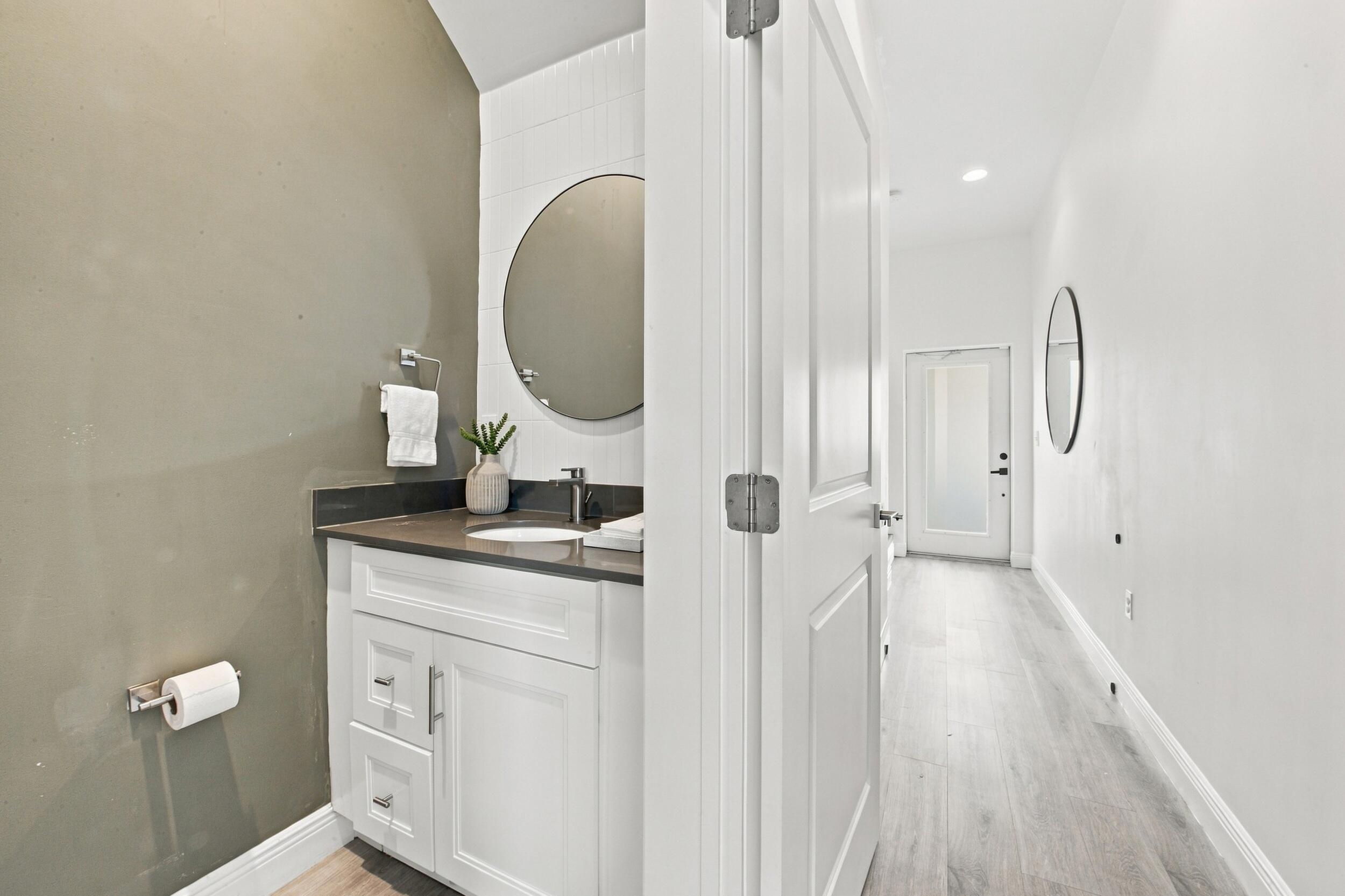 Powder room featuring a white vanity cabinet, solid surface countertop with an integrated basin, round wall-mounted mirror, and wood-finish flooring