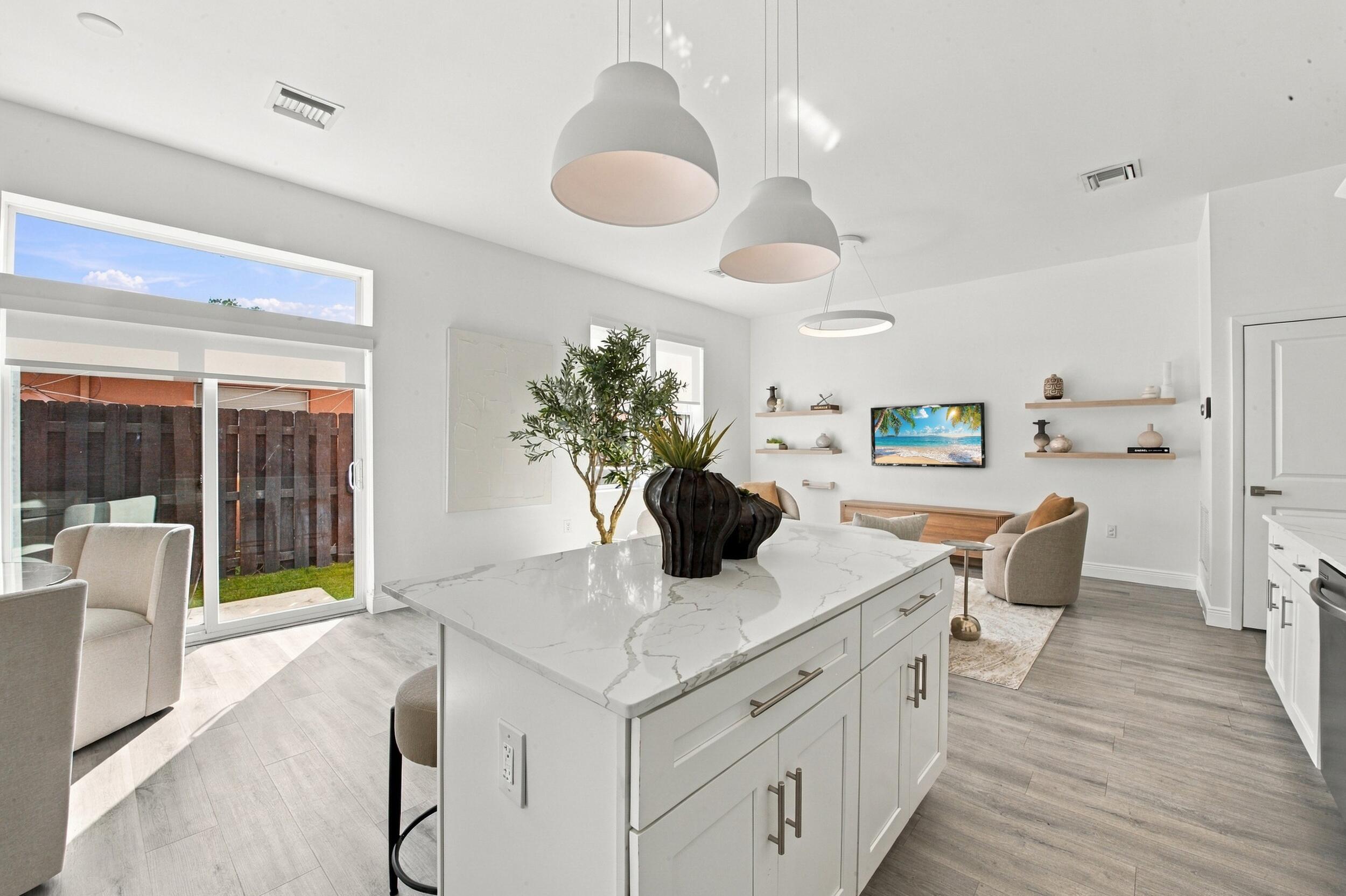 Kitchen featuring a central island with stone-patterned countertop, wood-finish flooring, white cabinetry, overhead pendant lighting, and sliding glass doors