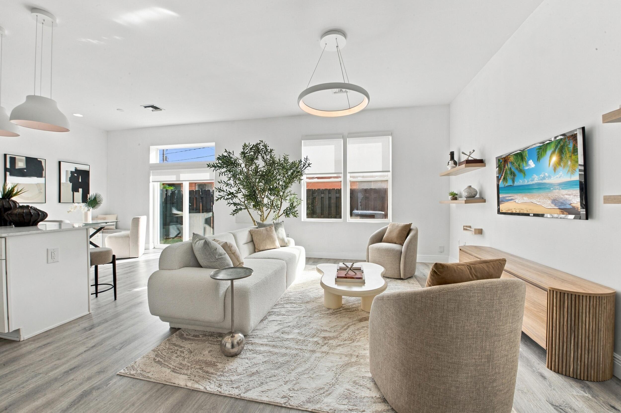 Open-concept interior featuring wood-finish flooring, modern circular pendant lighting, wood-finish wall shelving, and large windows Open-concept interior featuring wood-finish flooring, modern circular pendant lighting, wood-finish wall shelving, and large windows