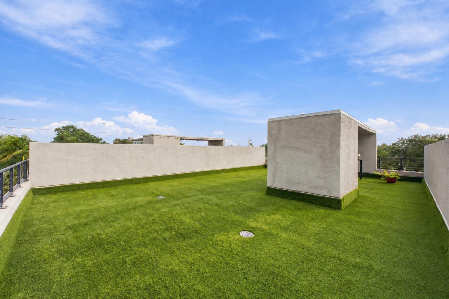 Expansive rooftop terrace featuring synthetic turf flooring, stucco-finished perimeter walls, and metal railings