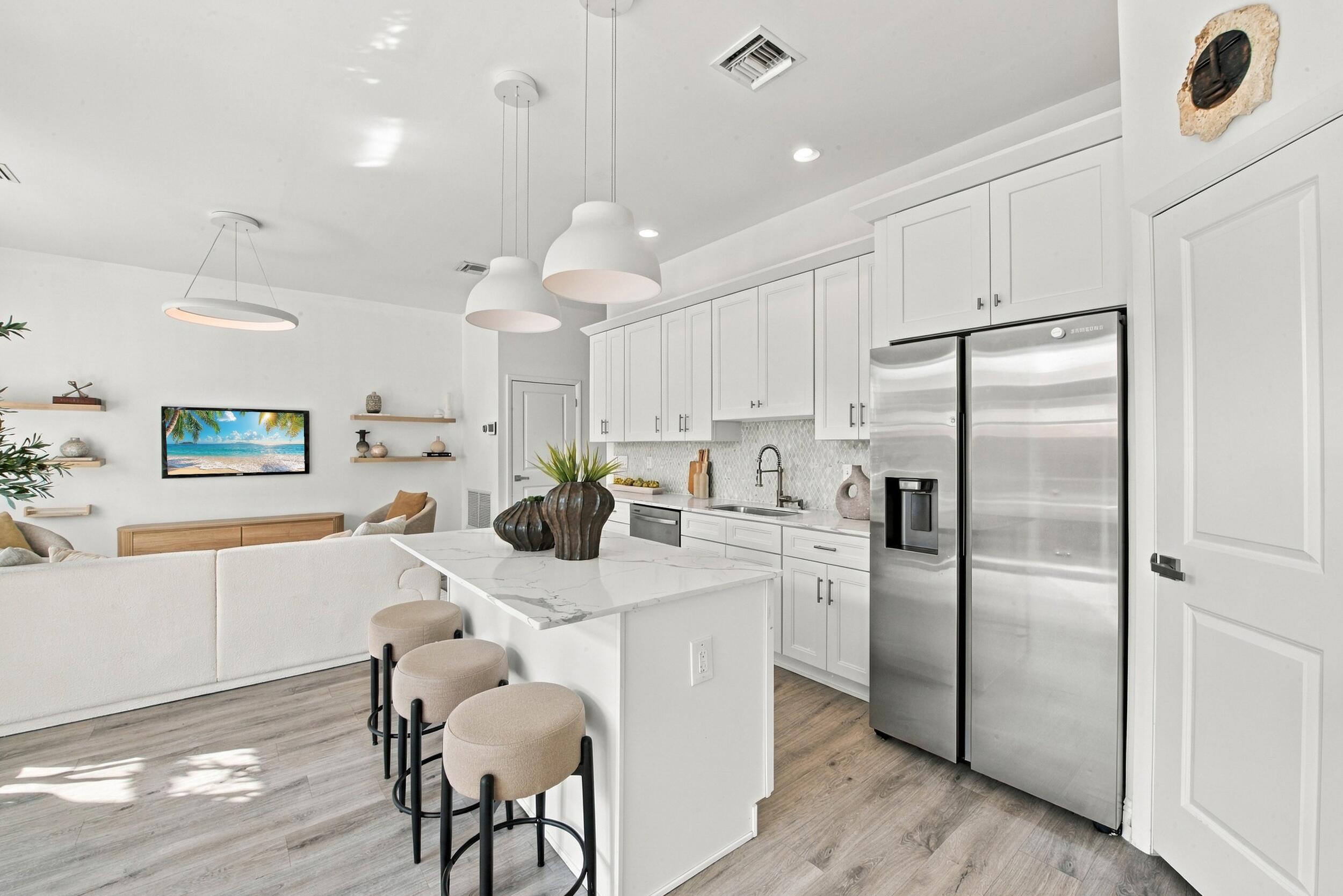 Kitchen featuring white shaker-style cabinetry, stone-finish countertops, stainless steel appliances, a center island with pendant lighting, and wood-finish flooring