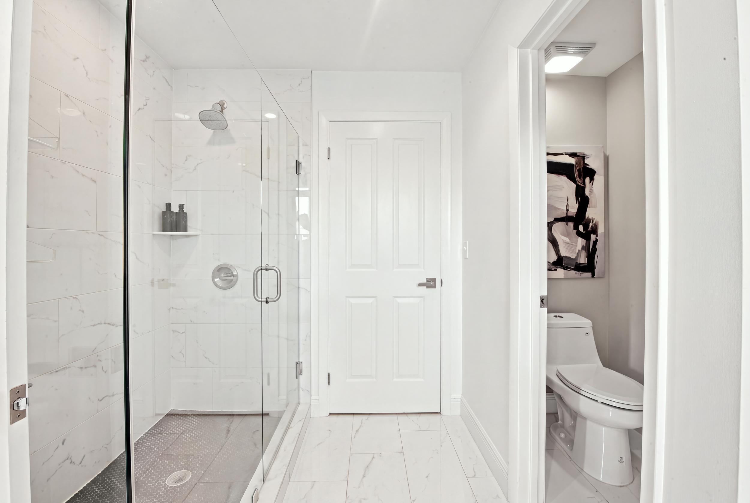 Walk-in shower with floor-to-ceiling stone-pattern tile, frameless glass enclosure, built-in shelving, and fixed shower head