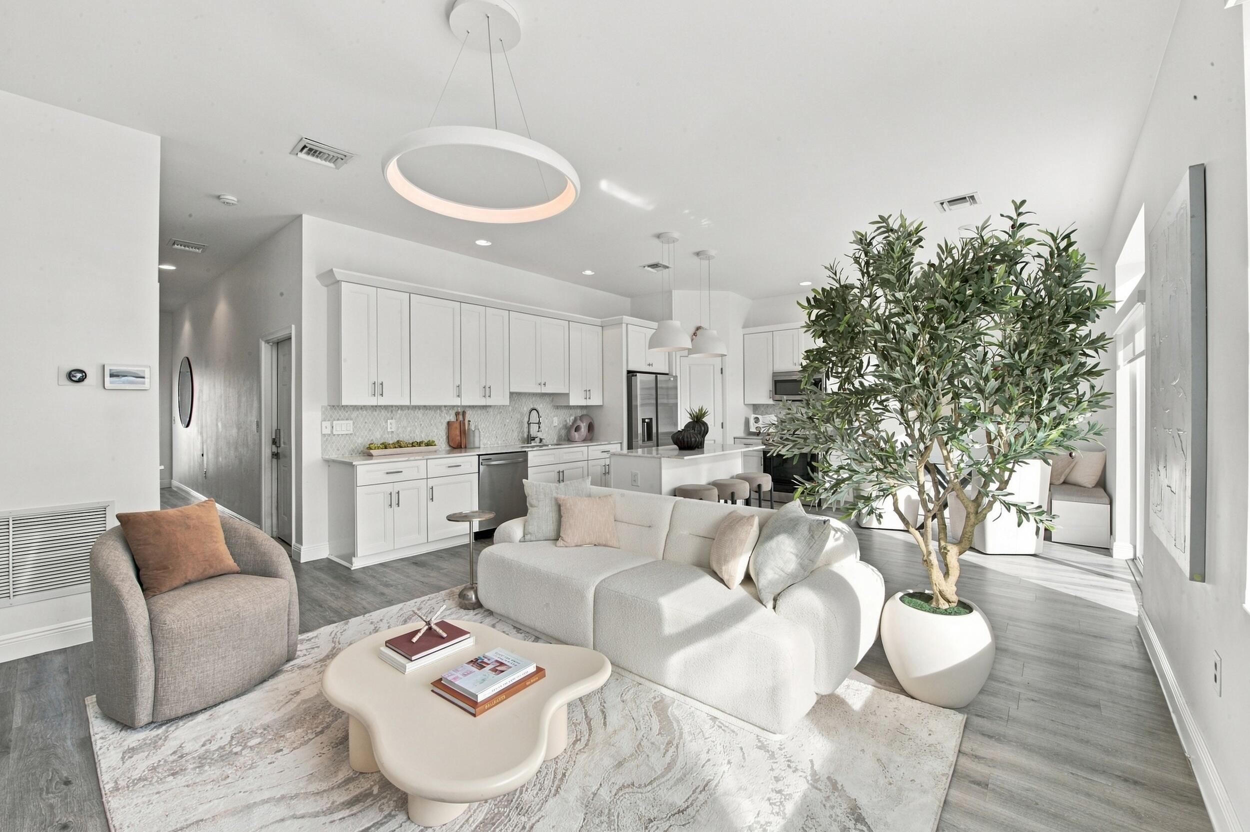Open-concept interior featuring wood-finish flooring, white shaker-style cabinetry, a central kitchen island, recessed lighting, and a modern circular pendant light fixture Open-concept interior featuring wood-finish flooring, white shaker-style cabinetry, a central kitchen island, recessed lighting, and a modern circular pendant light fixture