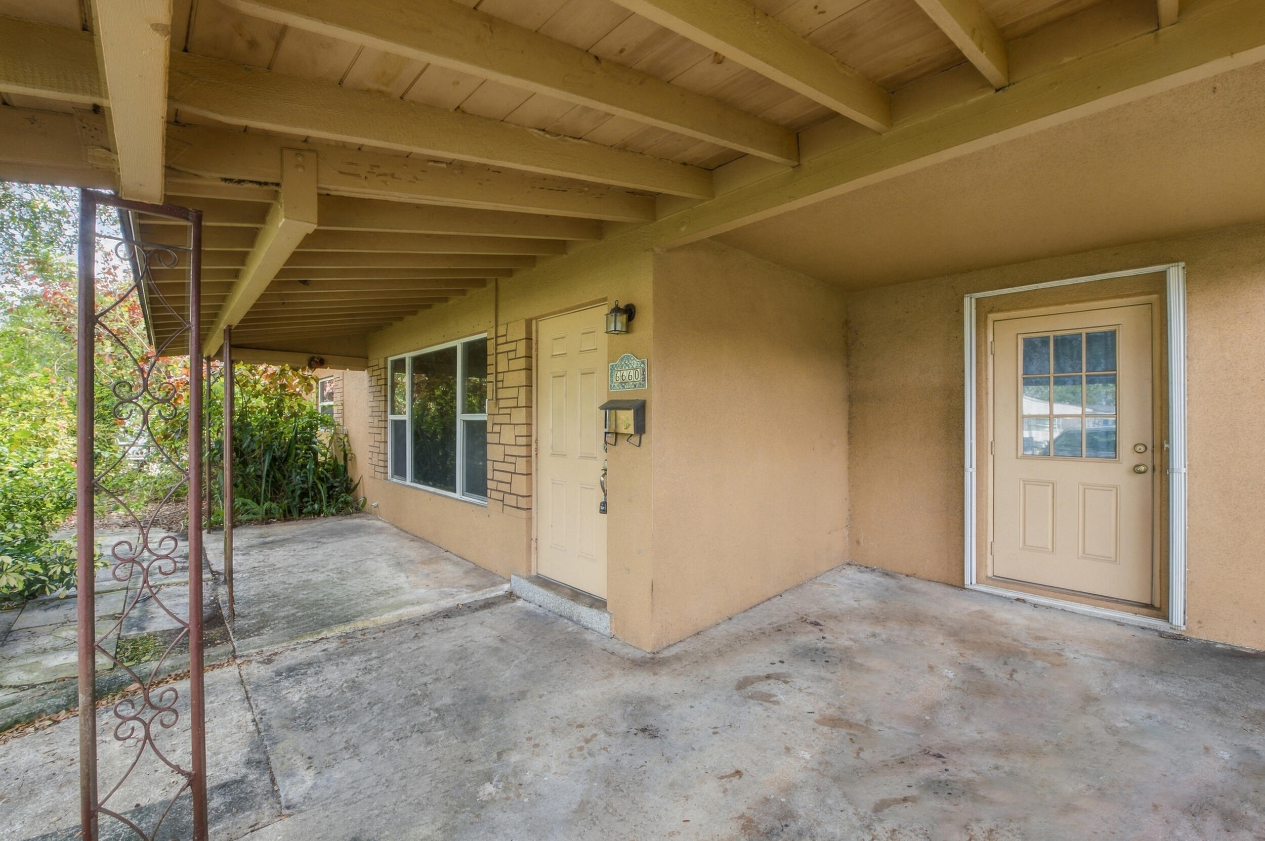 Covered entryway featuring a concrete porch, exposed beam ceiling, decorative metal support post, and dual exterior doors with multi-pane glass detailing