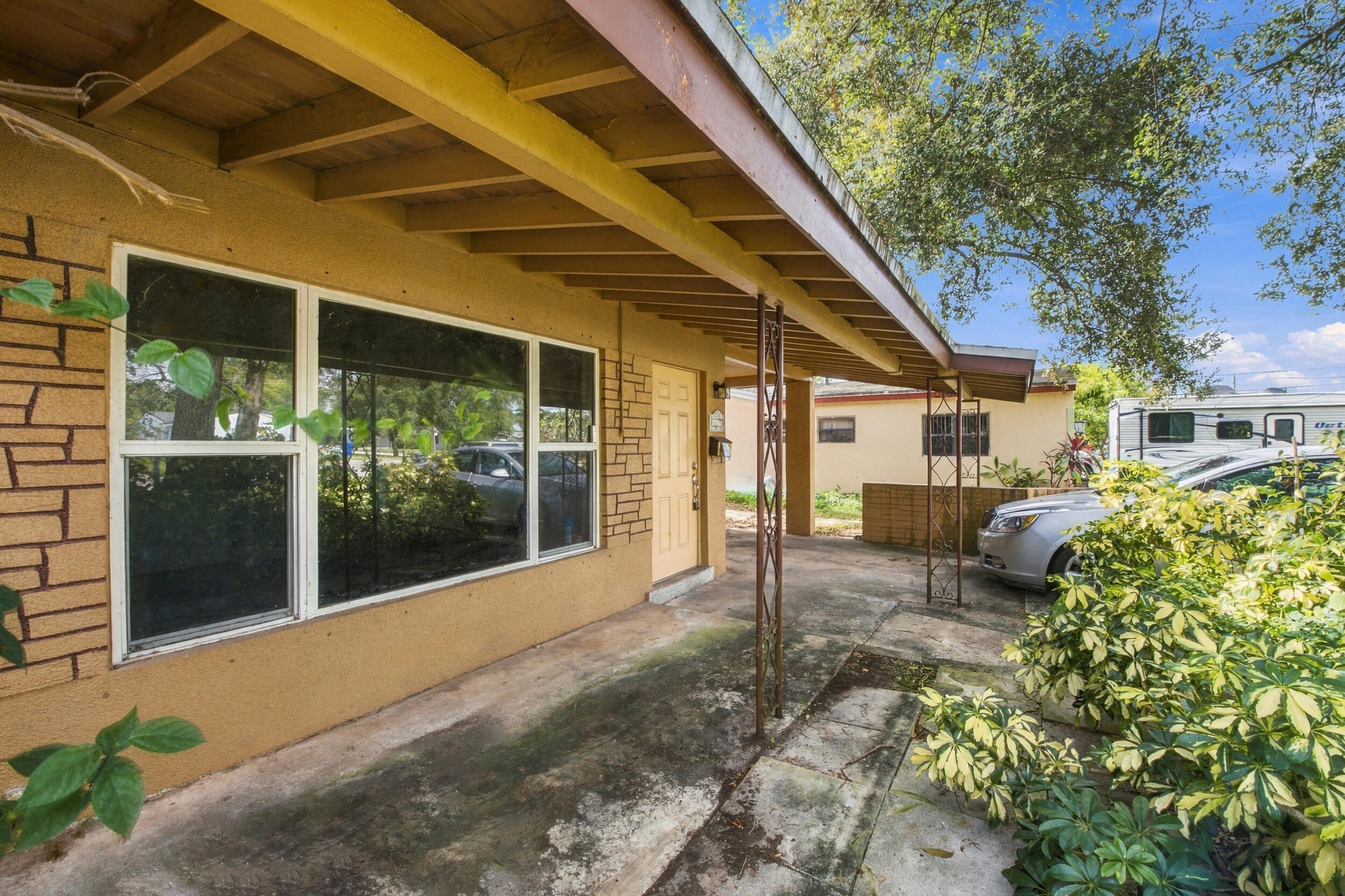 Exterior facade featuring textured stucco, stone-veneer accents, a covered concrete porch, and metal support posts