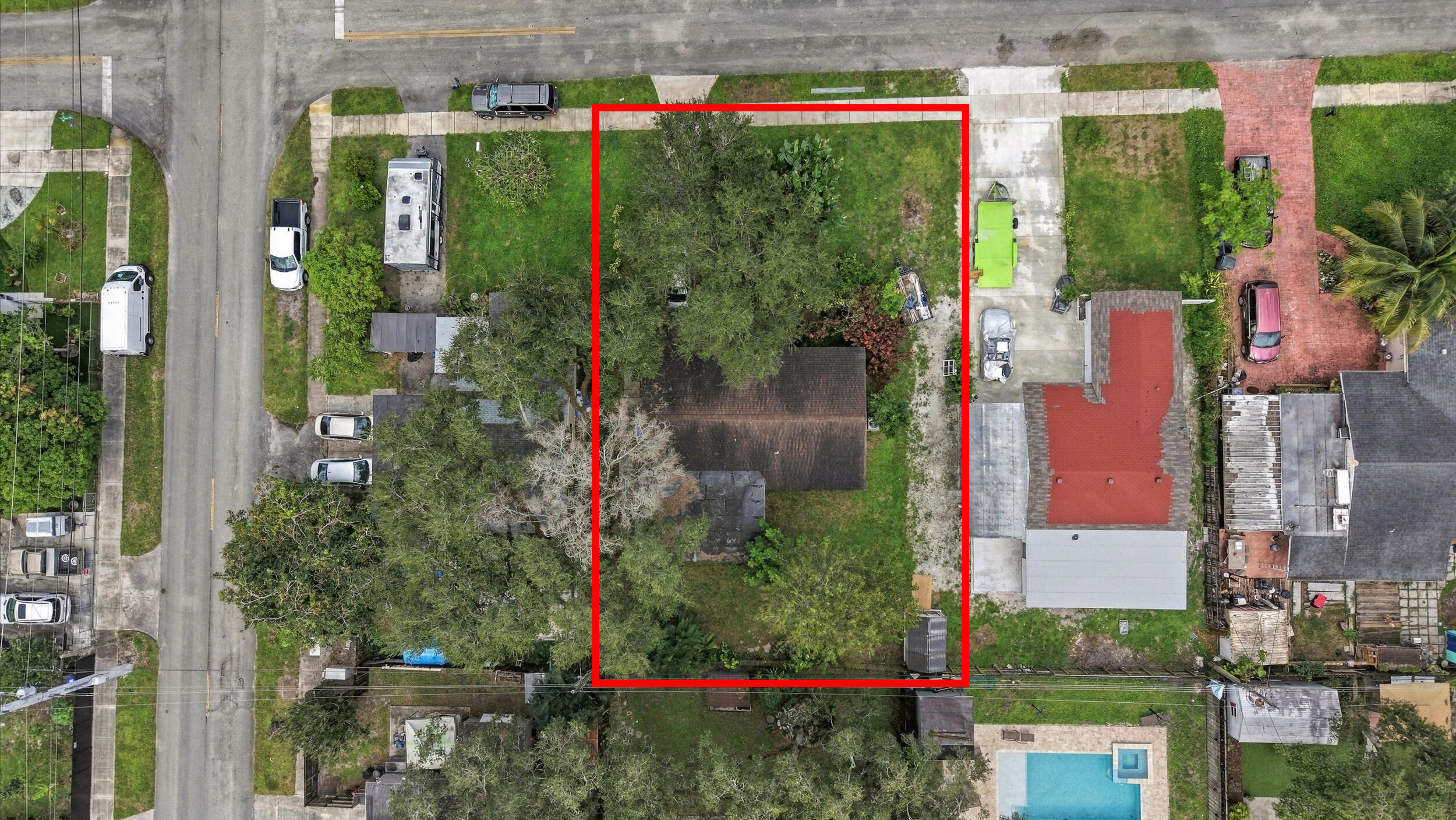 Aerial view of a rectangular corner lot featuring mature trees and a gravel driveway