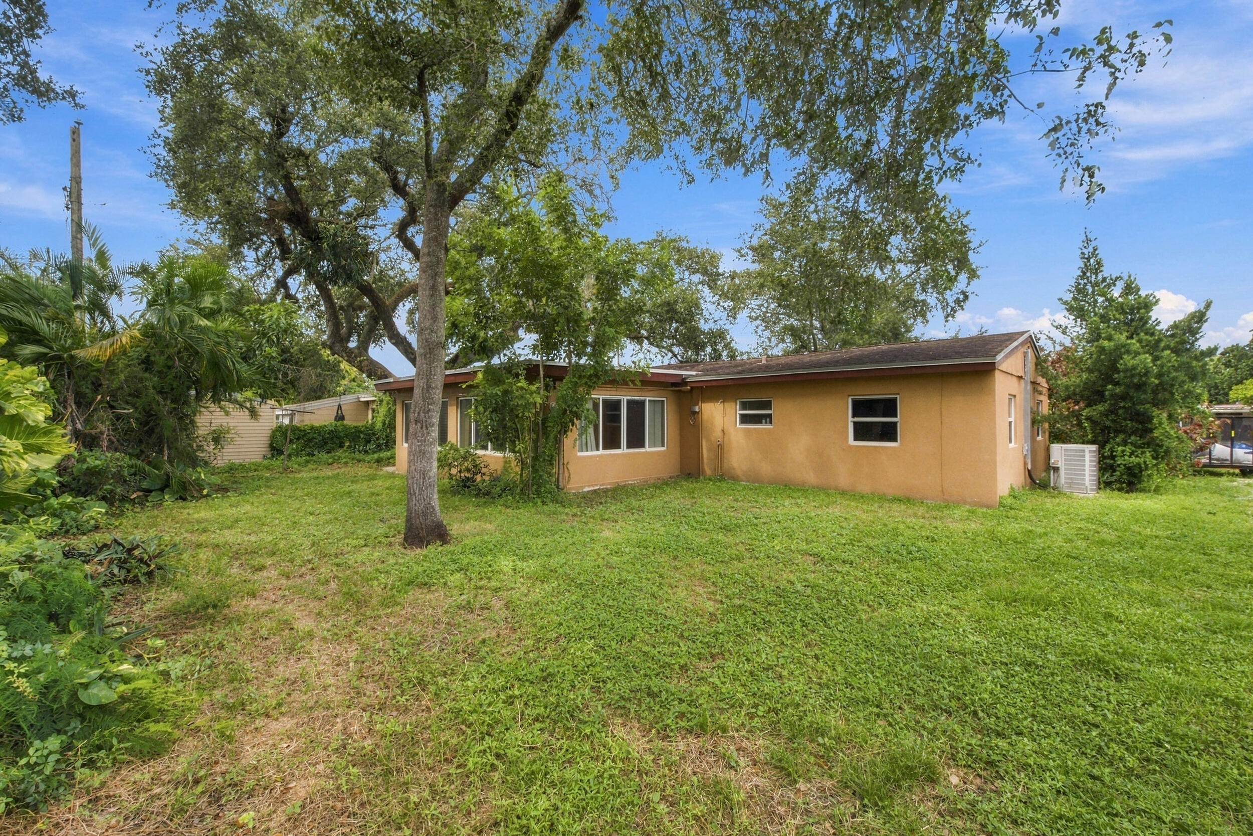 Single-story stucco exterior featuring multi-pane windows and mature trees set within a grass lawn