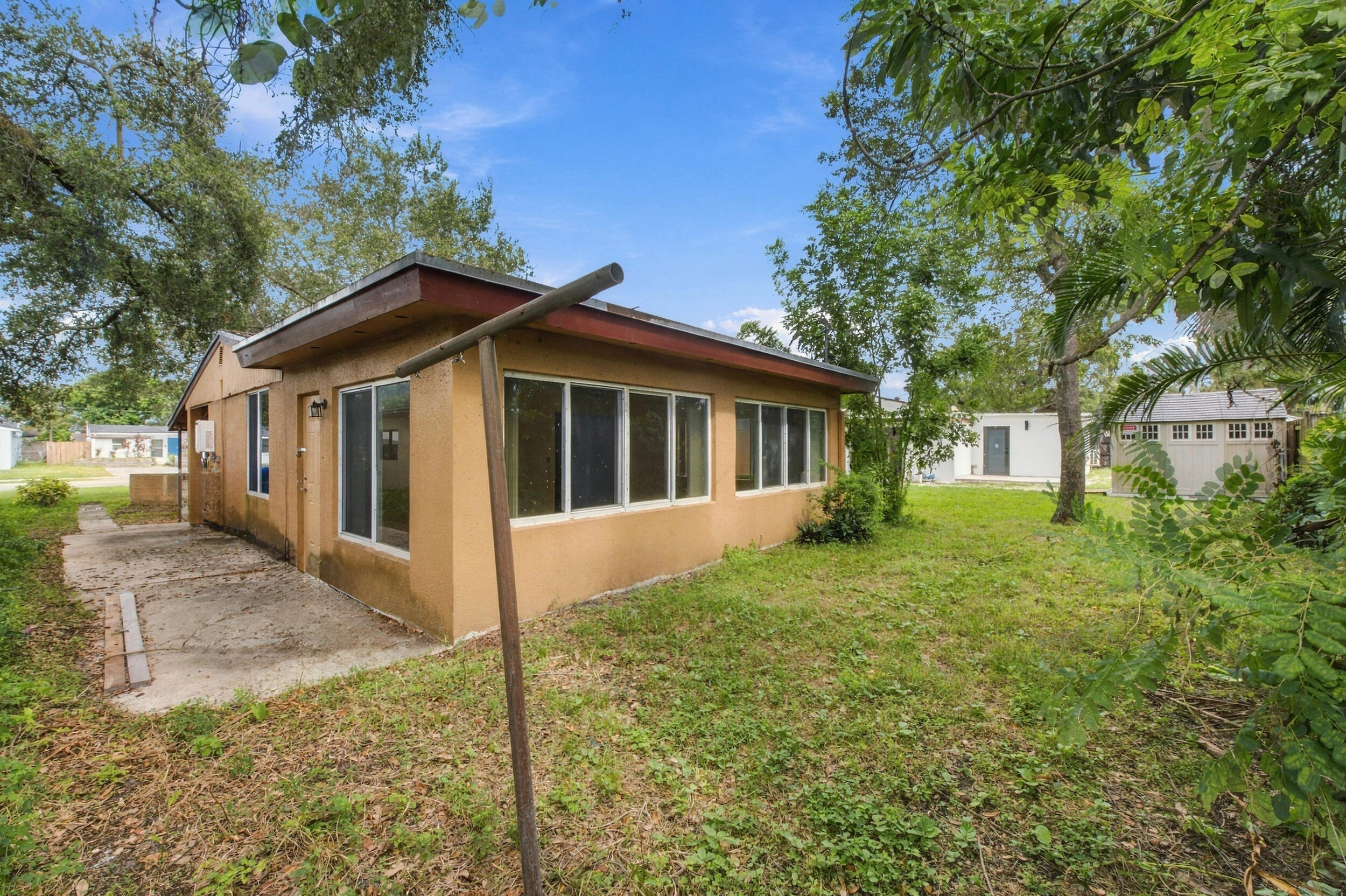 Stucco exterior featuring large windows, a concrete side patio, mature trees, and a detached structure