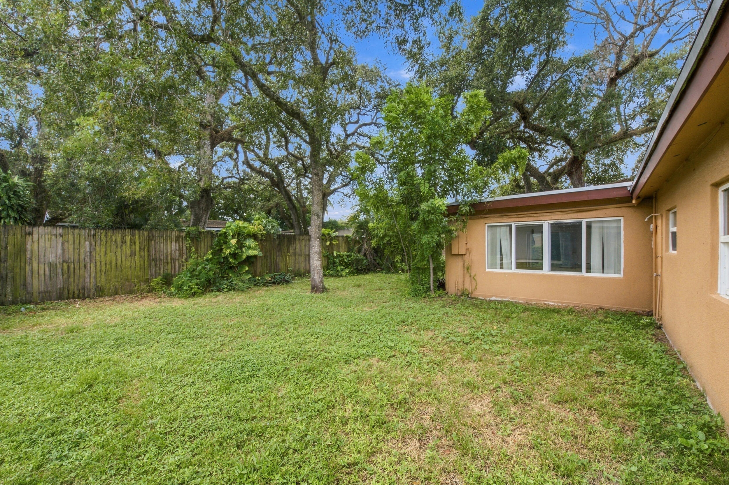 Backyard featuring a grass lawn, mature trees, and a wooden privacy fence