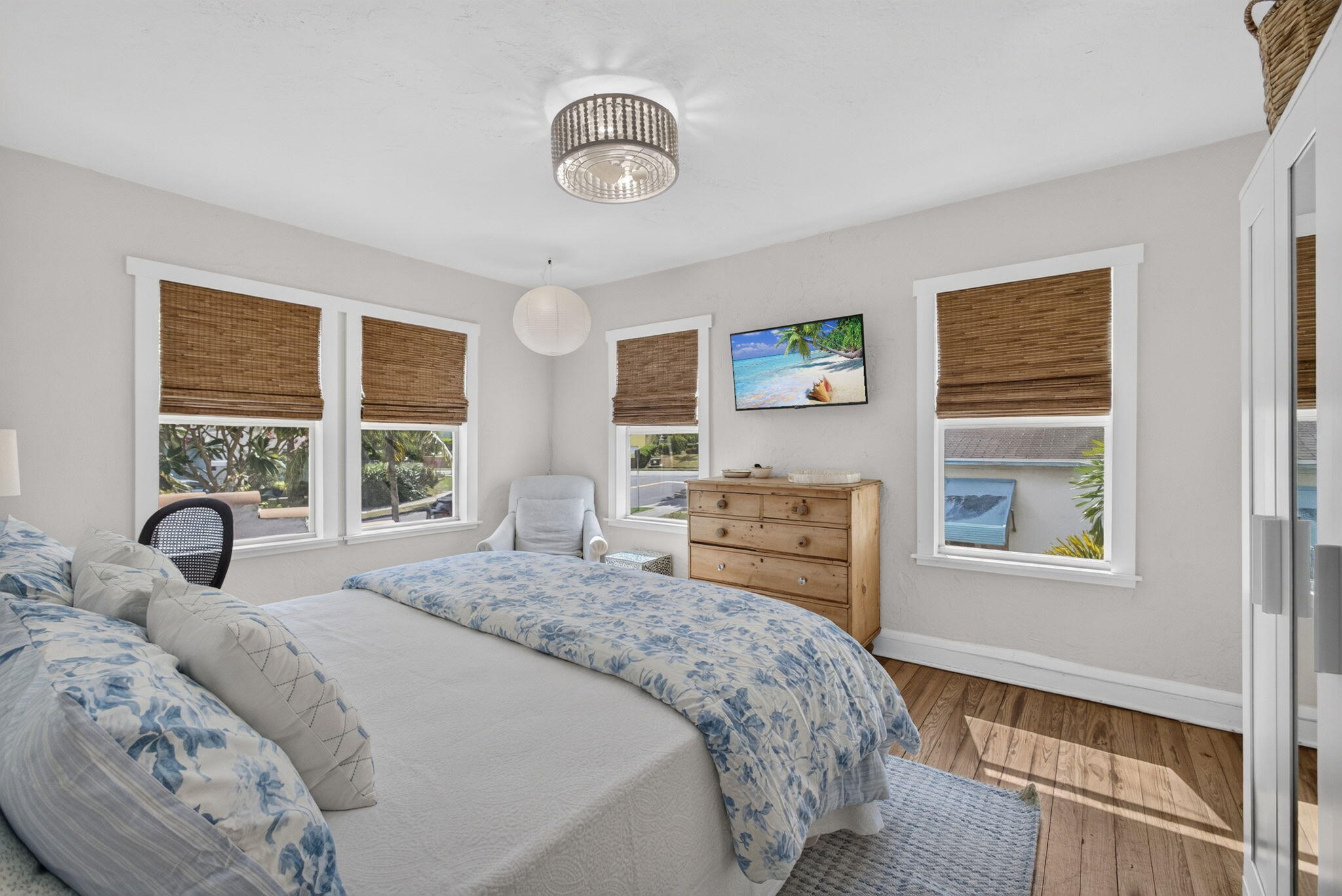 Room featuring wood-finish flooring, multiple windows with white trim, and a decorative drum-style ceiling light fixture